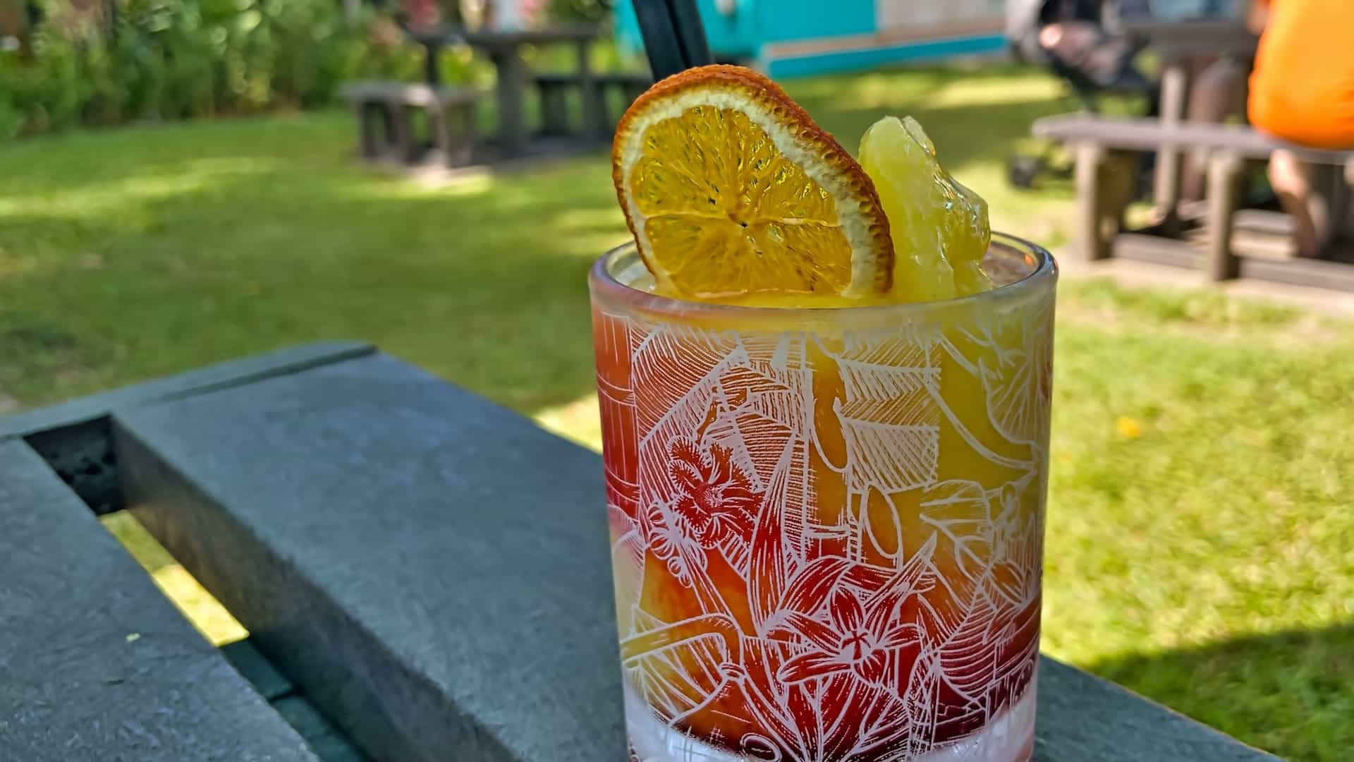 A colorful, chilled rum cocktail served in a glass, likely made with local Takamaka Rum, resting on a wooden table at the distillery's bar in Mahé, Seychelles. The drink is garnished with fresh fruit or a lime slice.