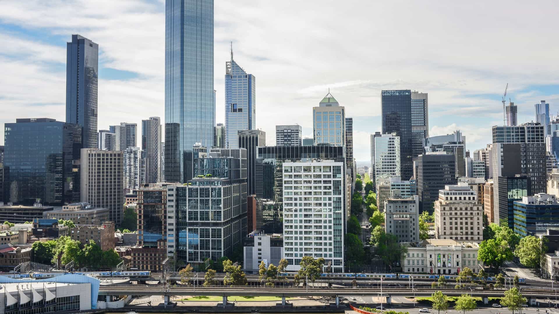 A scenic photograph of the Southbank precinct in Melbourne, Australia, captured along the Yarra River. The image likely features a view across the river towards the tall buildings of the Melbourne central business district (CBD) skyline, including prominent skyscrapers like the Eureka Tower or Australia 108. In the foreground, the Southbank Promenade is visible, bustling with pedestrians, and potentially featuring outdoor dining areas or the river's edge with various boats or ferries. The overall scene captures the vibrant, modern urban atmosphere of Melbourne's riverside.