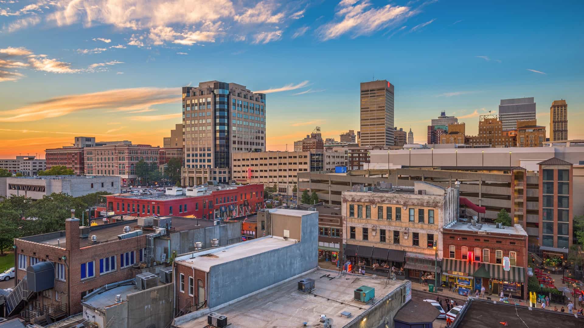 A stunning panoramic photograph showcasing the Memphis, Tennessee, USA downtown cityscape at dusk, looking over the famous Beale Street entertainment district, with the brilliant lights of the high-rise buildings reflecting upon the Mississippi River.