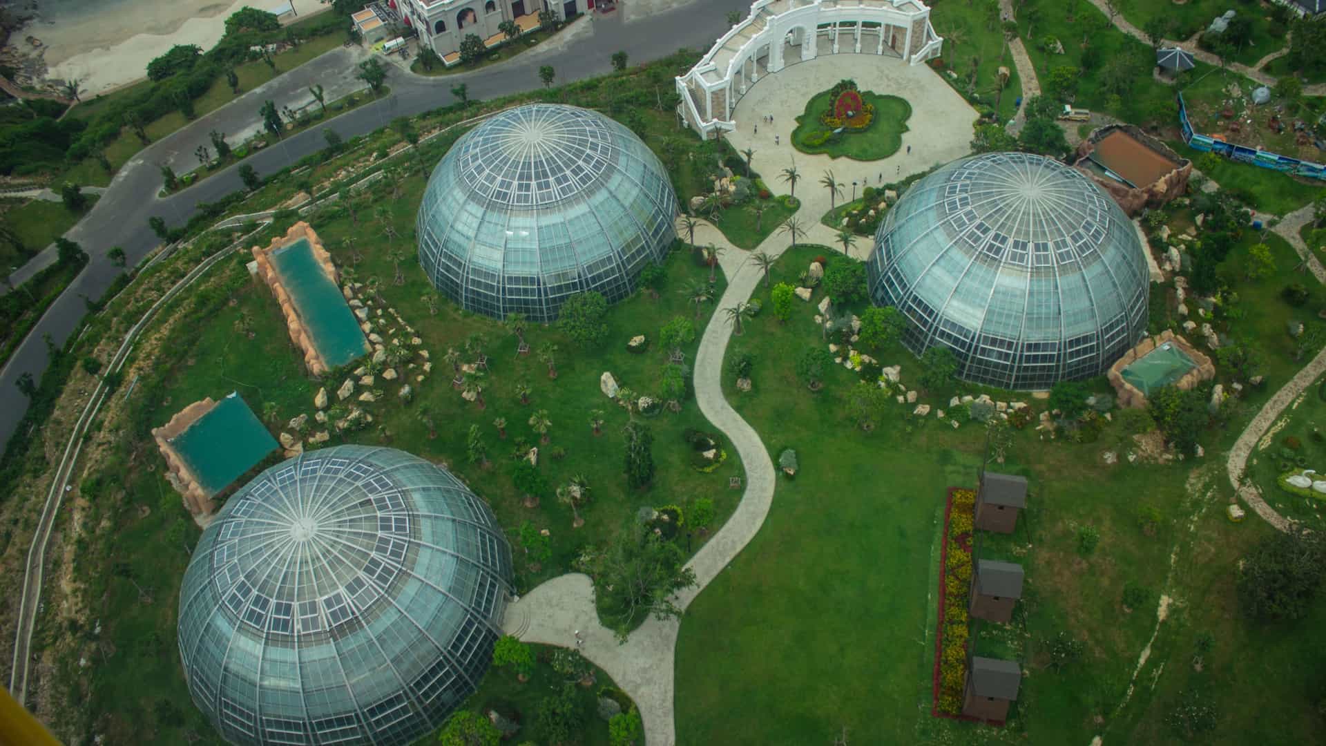 An exterior view of the Mitchell Park Horticultural Conservatory in Milwaukee, Wisconsin, featuring its three iconic, beehive-shaped, conoidal glass domes against a blue sky.