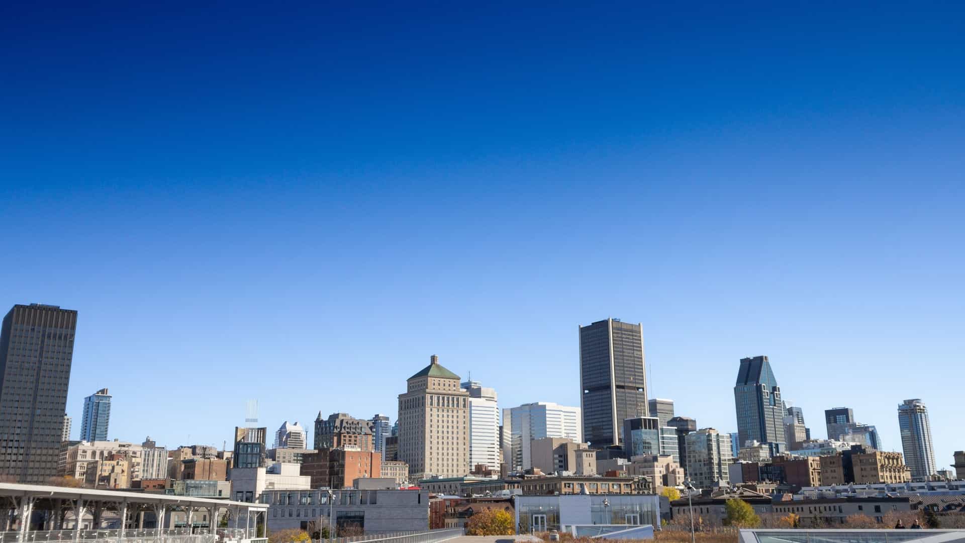 A view of the skyline of Old Montreal, showcasing a blend of historic and modern architecture. In the foreground are the iconic historic buildings of Vieux Montréal with their distinctive facades, while the background features the sleek, towering skyscrapers of the city's Central Business District (CBD). The image captures the contrast and coexistence of the old and new parts of the city.