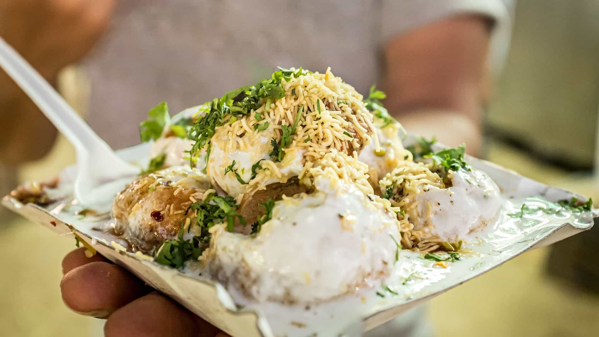 A close-up of Dahi Puri, an Indian street food chaat, with puris topped with yogurt, chutneys, sev, and coriander, ready to be served.