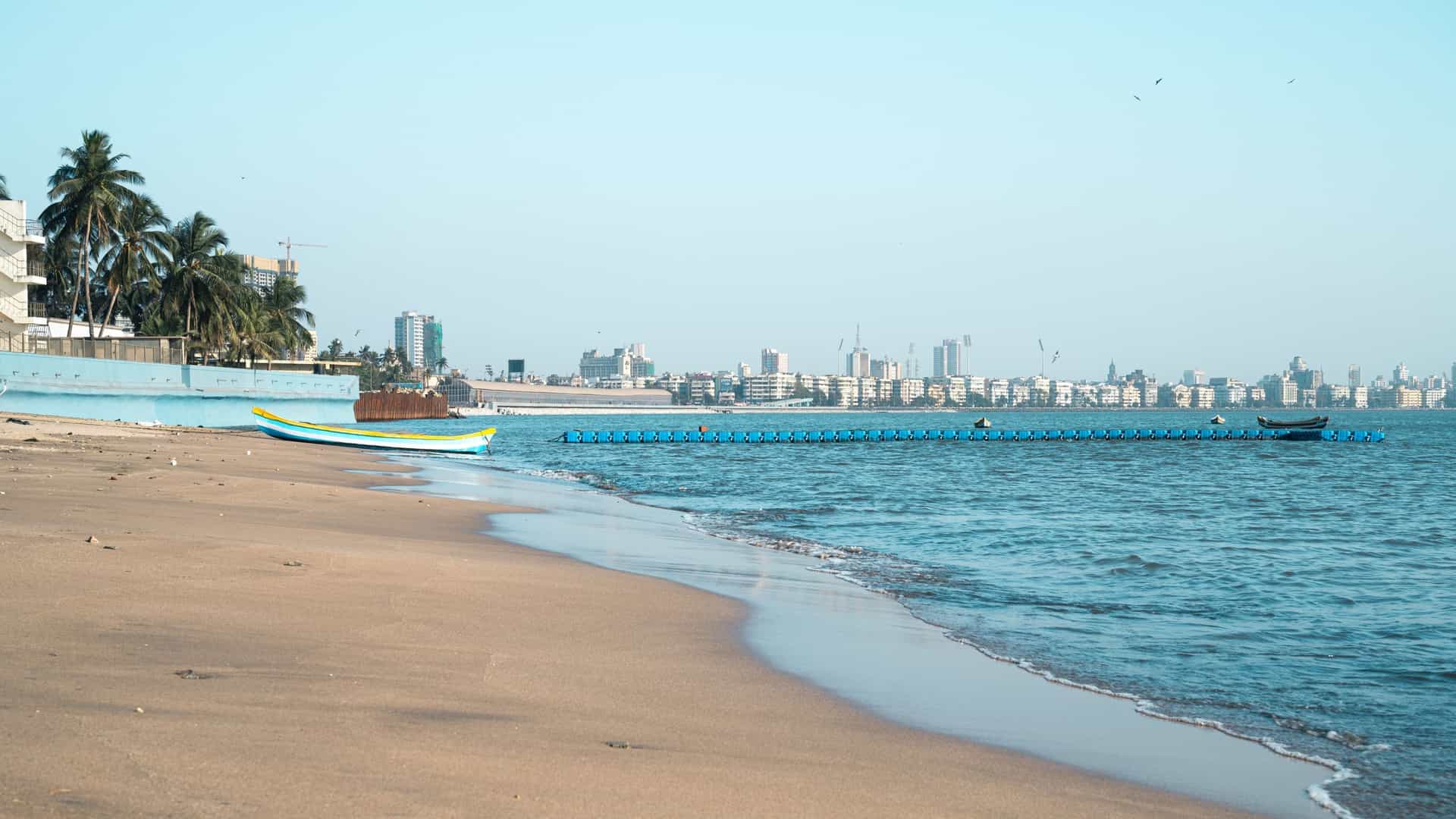 The Juhu Beach coastline and high-rise skyline in Mumbai, India, at sunset, showcasing the wide beach and numerous buildings under a colorful evening sky.