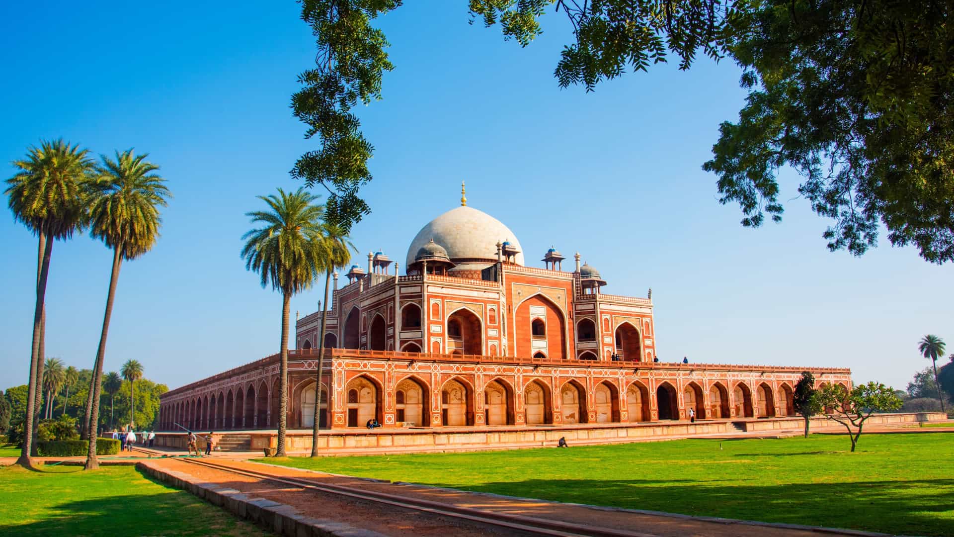 The majestic Humayun's Tomb, the mausoleum of the Mughal Emperor Humayun, stands in Delhi, India. The architecture features a large structure made of red sandstone and white marble, topped with a prominent double-dome, and is set within the symmetrical, lush green Charbagh garden.