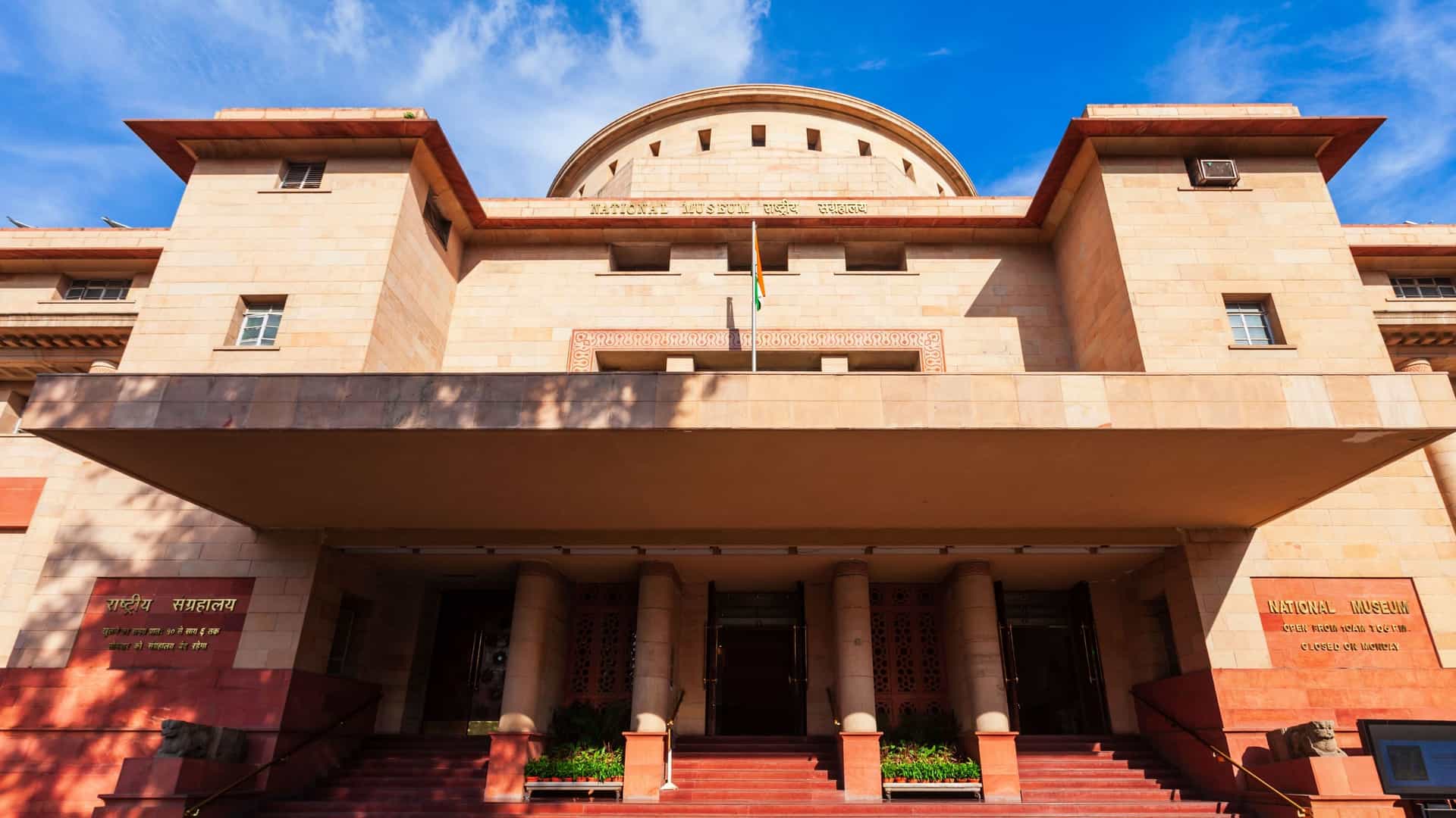 A daytime photo of the National Museum in New Delhi, India. The large, stone building is located on the corner of Janpath and Maulana Azad Road and is one of the largest museums in the country. It was established in 1949 and houses a vast collection of art and artifacts covering over 5,000 years of Indian cultural heritage.