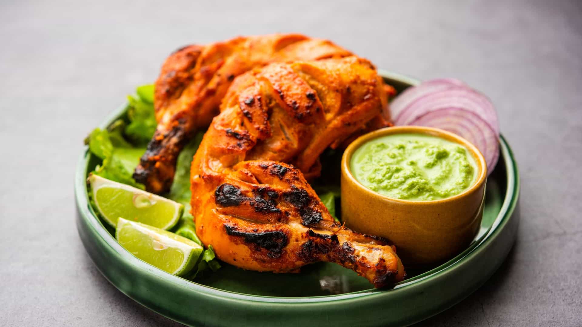 A dish of Tandoori chicken, which is prepared by roasting chicken marinated in yogurt and spices in a tandoor (a clay oven). The chicken is typically served with sliced onion and a green chutney.