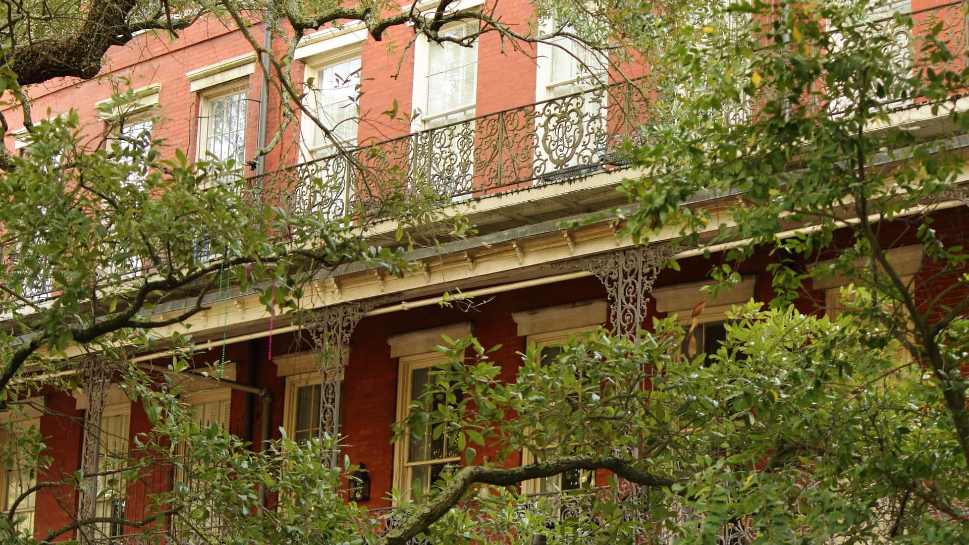 A view of the New Orleans French Quarter, known for its unique and historic architecture. The buildings feature intricate wrought iron balconies, which are a prominent characteristic of the neighborhood's Creole and Spanish influenced design. The street below is lined with shops and streetlights.