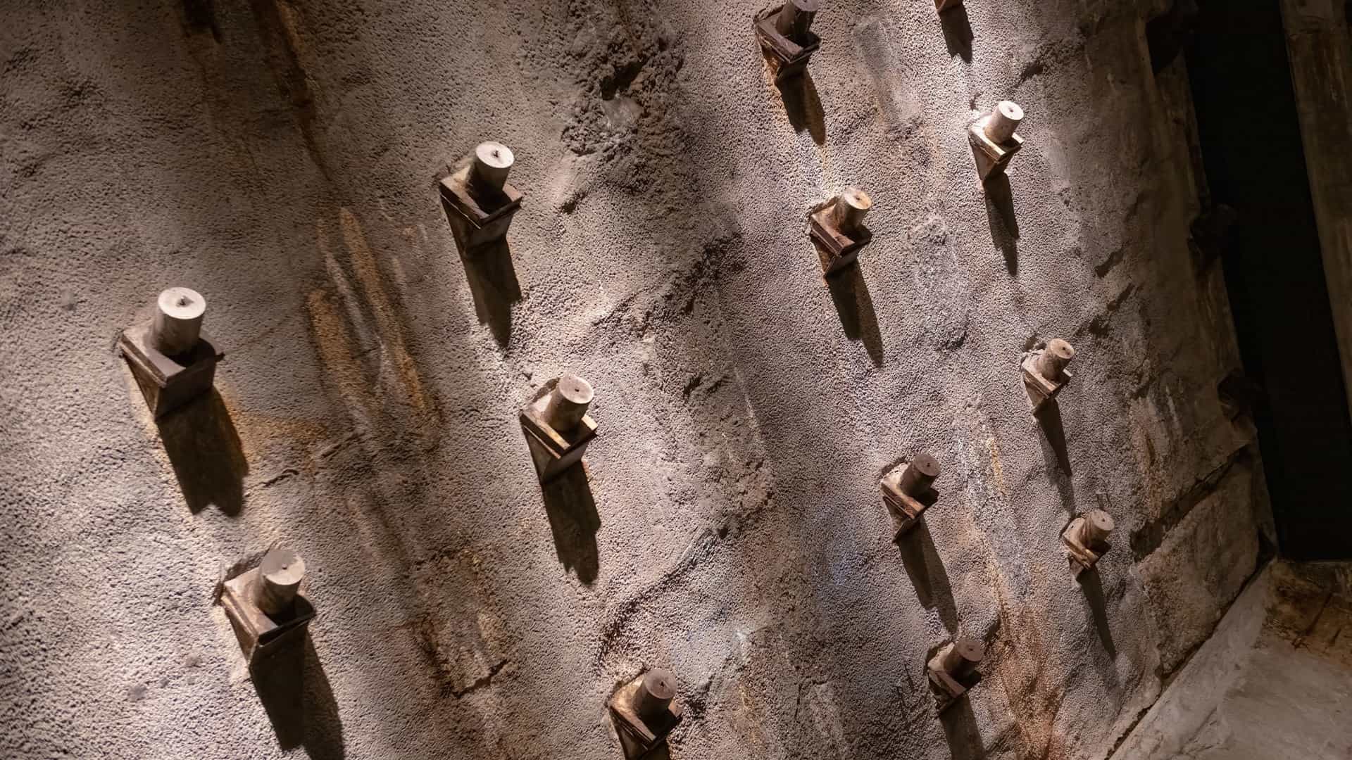 A textured, sloped concrete wall with rows of protruding metal bolts, suggestive of foundational or tunnel construction in New York.