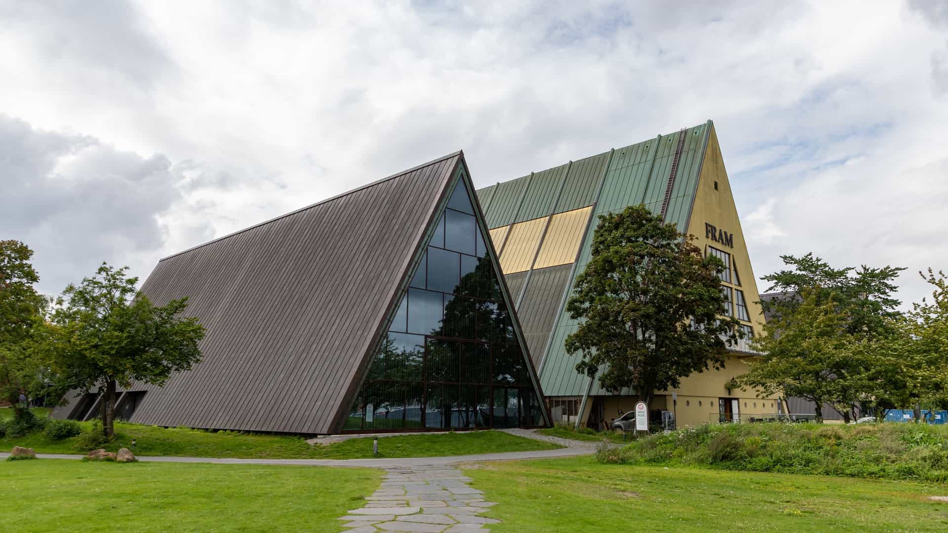 The interior of the Fram Museum in Oslo, Norway. The museum's main exhibit, the polar exploration ship Fram, is prominently featured, enclosed within a large, modern glass and metal structure. Visitors are visible on the decks of the ship and on the surrounding walkways, providing a sense of scale. The ship's wooden hull, ropes, and various nautical details are clearly visible. The overall scene is a testament to maritime history and polar exploration.