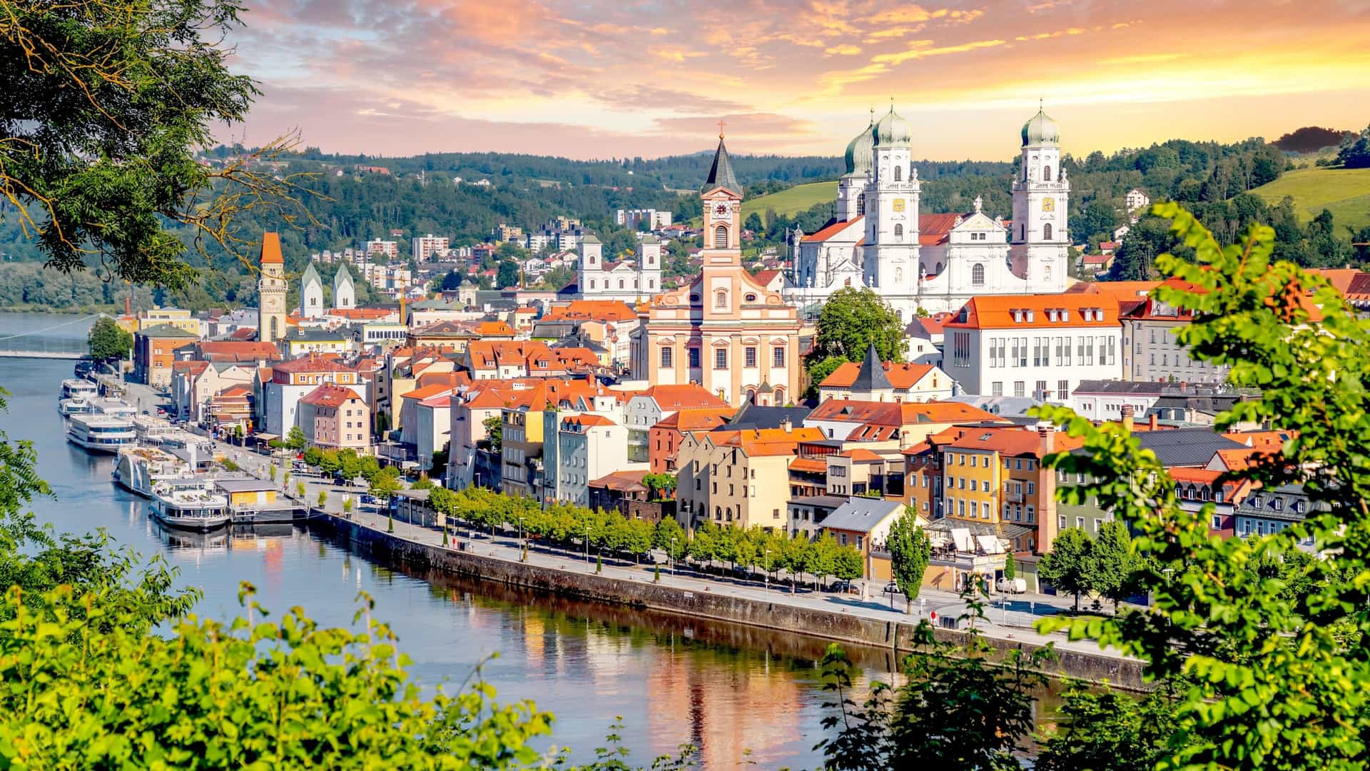 An aerial view of the historic old city of Passau, Bavaria, Germany. The city is situated at the confluence of three rivers, and its baroque buildings with winding alleys are visible below a prominent cathedral.