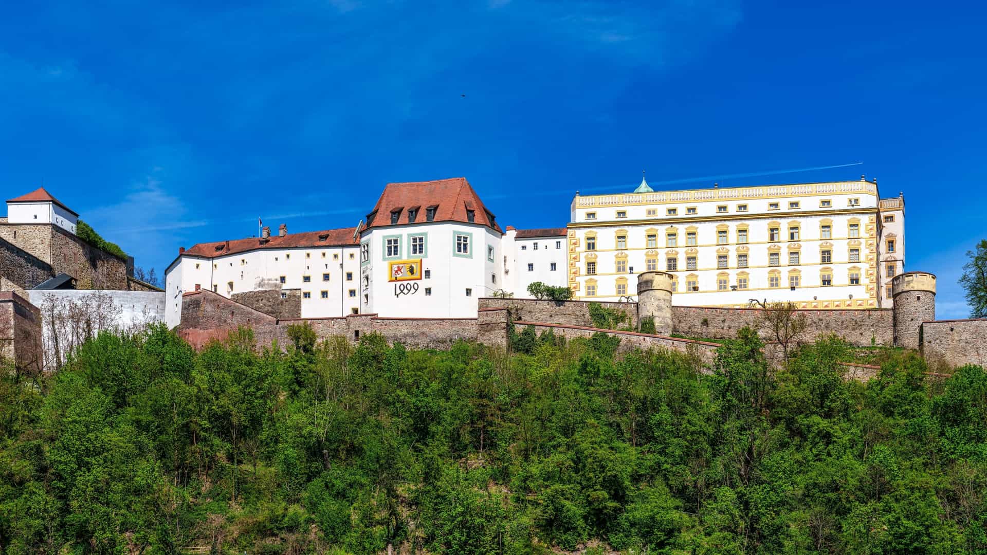 An exterior view of Veste Oberhaus, a medieval fortress perched on a hill above the old town of Passau, Germany. The fortress, which now houses a museum, overlooks the confluence of the Danube and Ilz rivers.
