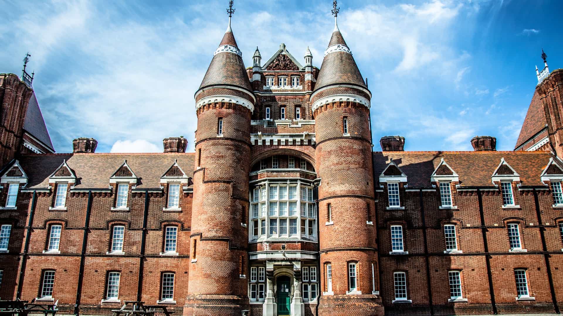 A frontal view of the Portsmouth Museum and Art Gallery, housed in a large, imposing red-brick Victorian building. The symmetrical facade features two prominent, rounded corner towers with conical roofs, and a central bay with stacked bay windows, all characteristic of the historic Royal Naval Barracks architecture.
