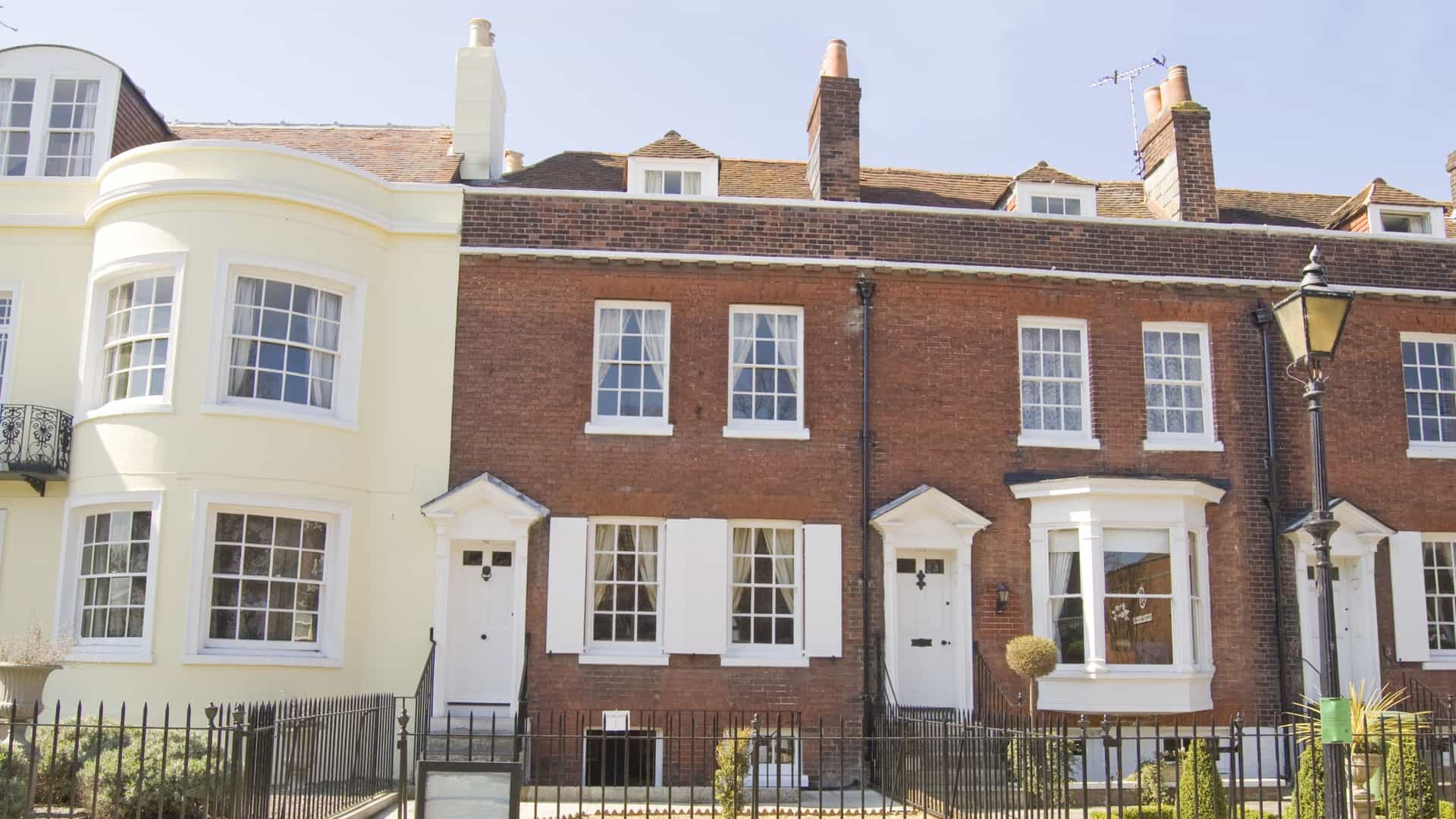 A clear photograph of the birthplace of Charles Dickens in Portsmouth, Hampshire, England. The historic Georgian house is a three-story red brick building with white trim, a black front door, and a prominent commemorative blue plaque mounted on the facade to mark its historical significance. The building is situated on a quiet residential street.