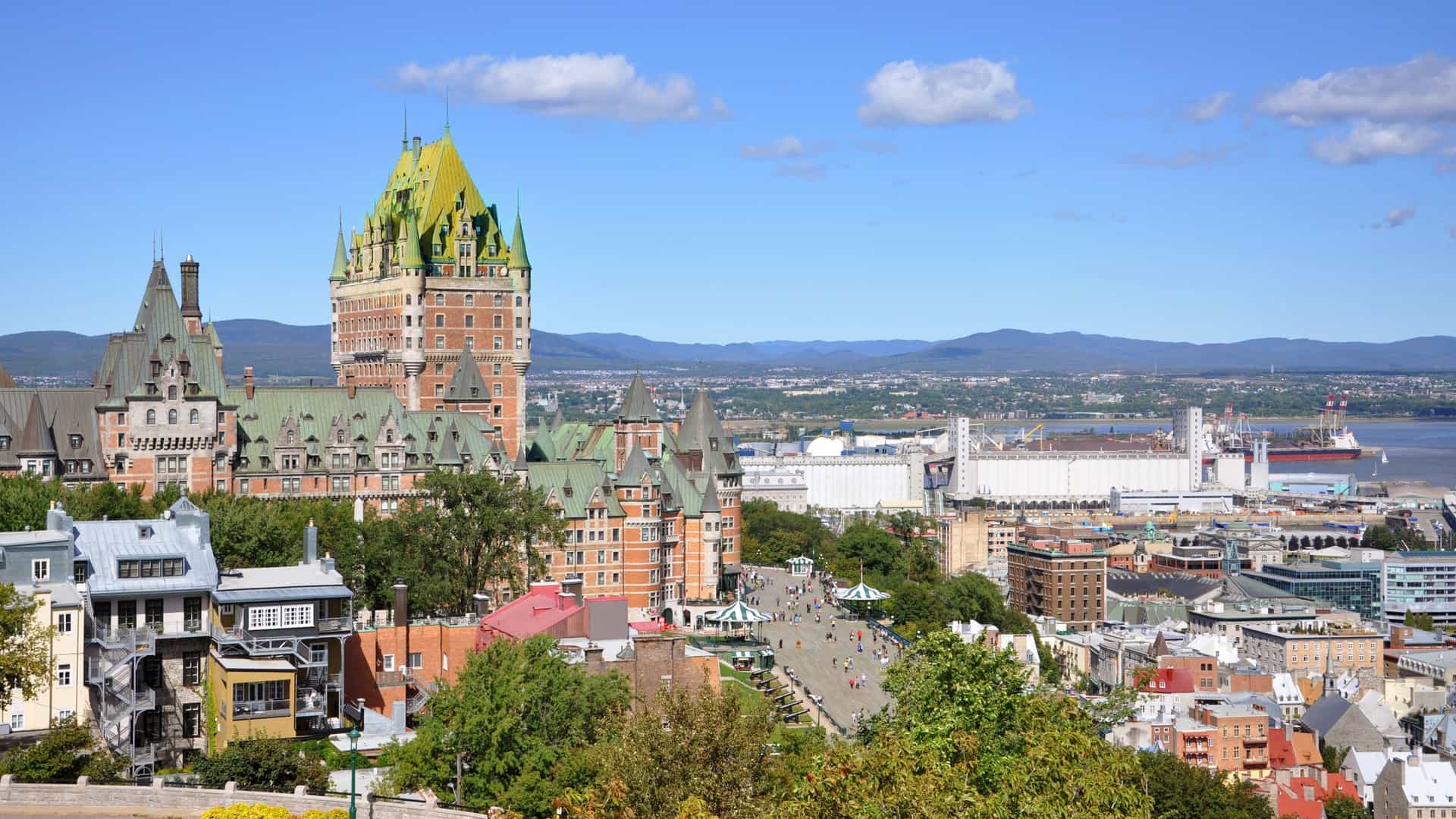 A panoramic view of the Old Quebec City skyline, dominated by the iconic, Châteauesque style Fairmont Le Château Frontenac hotel with its copper roof and steep turrets, positioned atop Cape Diamond and overlooking the Saint Lawrence River.