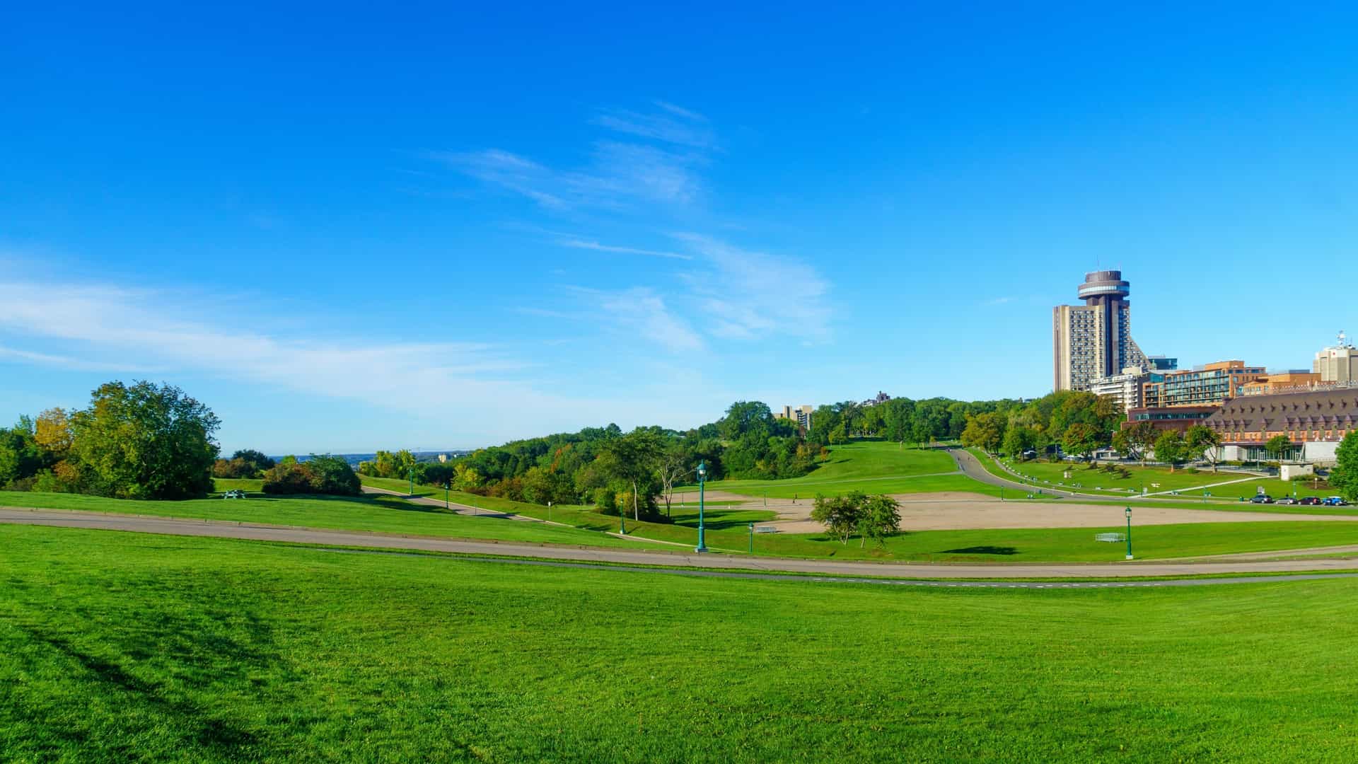 A scenic, wide angle view of the expansive Plains of Abraham Park in Quebec City, Canada, showing a large, grassy field with gently rolling hills and scattered trees. The urban park is a historic site and a prominent green space in the city.