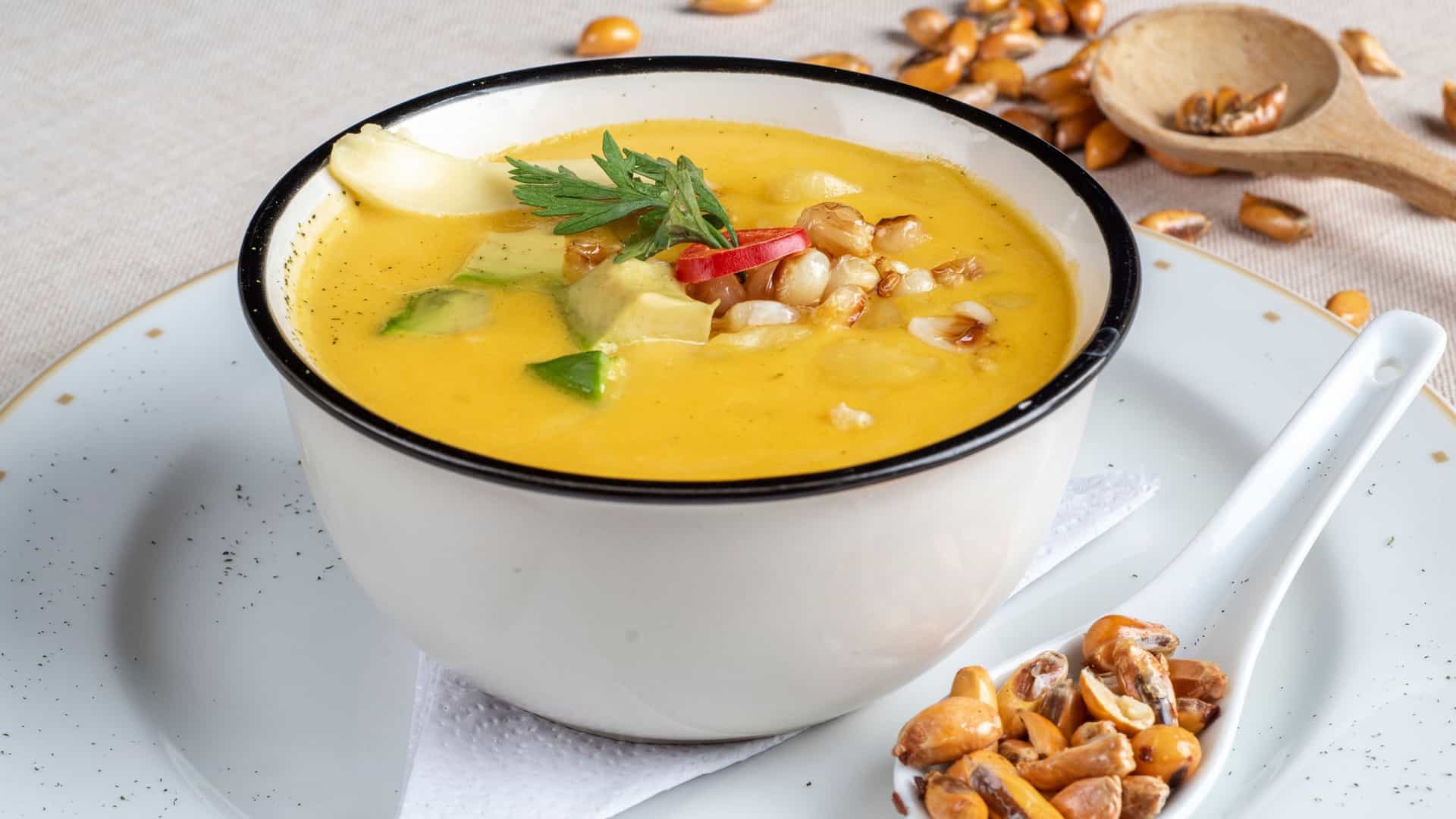 A close-up of a bowl of Locro de Papa, a hearty, creamy, yellow-colored Ecuadorian potato soup/stew. The soup is typically made with potatoes, cheese (queso fresco), milk, and seasoned with achiote (annatto), which gives it its distinct color. The soup is usually garnished with slices of fresh avocado, crumbled cheese, and chopped cilantro. It is a staple dish, particularly in the Andean highlands of Ecuador.