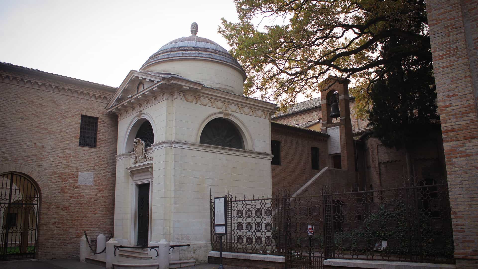 A view of Dante's Tomb in Ravenna, Italy, a small, square, neoclassical temple. The monument, designed by Camillo Morigia and built in 1781, features a domed roof and is situated in a tranquil area known as the "Zone of Silence" next to the Basilica of San Francesco. It is the final resting place of the great Italian poet, Dante Alighieri.