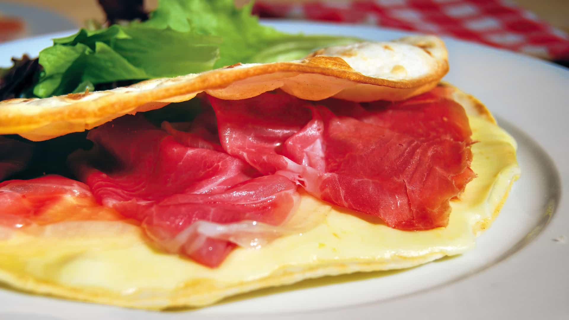 Delicious Italian piadina flatbread filled with melted cheese and speck ham, served warm on a plate with a fresh salad garnish.