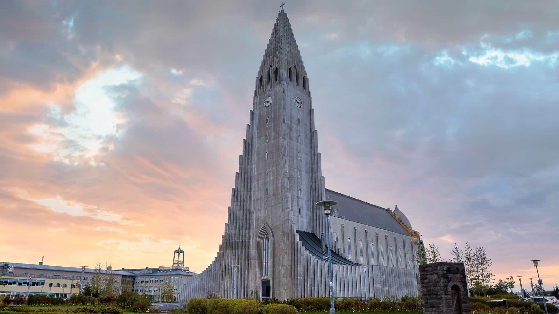 The iconic Hallgrímskirkja church in Reykjavik, Iceland, a tall, white concrete structure with a distinctive facade that features geometric columns inspired by Iceland's natural basalt formations. The statue of Leif Erikson stands in the plaza in front of the church.