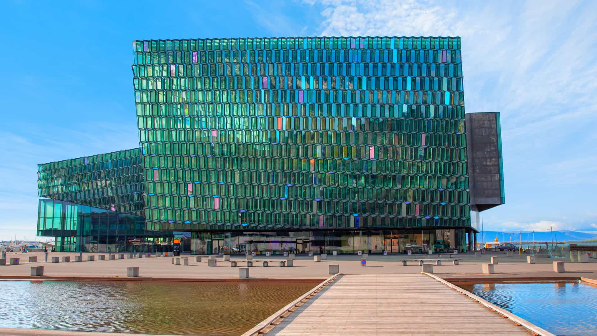 Low-angle view of the Harpa Concert Hall in Reykjavik, Iceland, showcasing its iconic, multi-faceted glass façade designed by Ólafur Elíasson and Henning Larsen Architects to resemble Iceland's natural basalt columns. The geometric glass panels reflect the light from the cloudy sky.