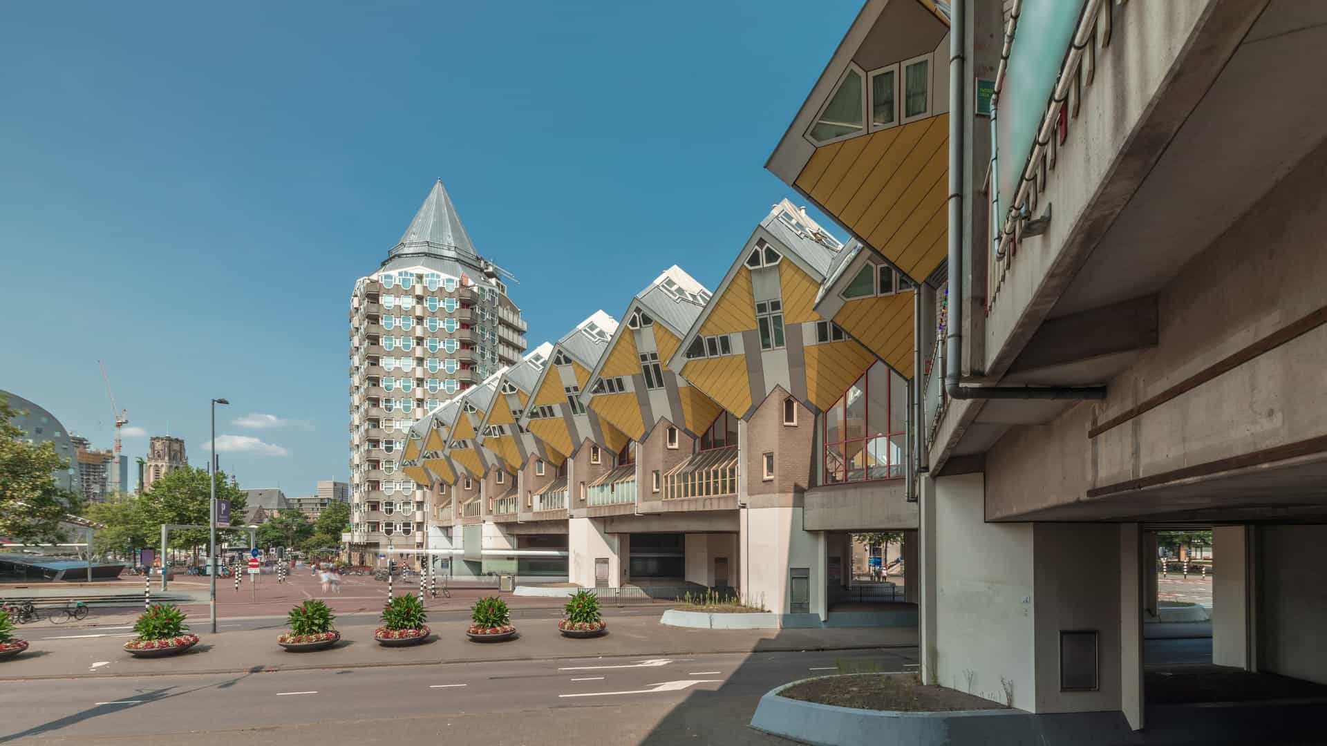 A close up view of the iconic bright yellow Cube Houses (Kubuswoningen) in Rotterdam, Netherlands. The unique, tilted cube shaped structures, which are residential units, are supported by hexagonal pylons and form a striking, angular architectural forest above a pedestrian walkway.