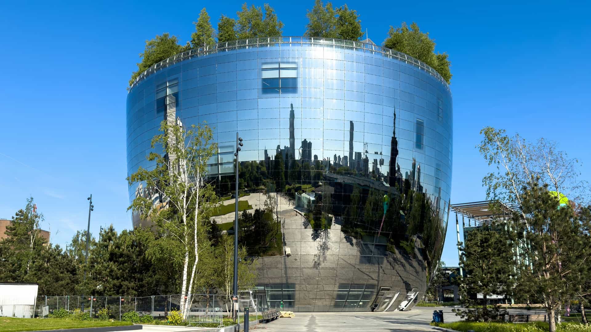 The Depot Boijmans Van Beuningen in Rotterdam, a large, ovoid building with a striking, highly reflective mirrored facade that reflects the surrounding green trees of the Museumpark and the city skyline.
