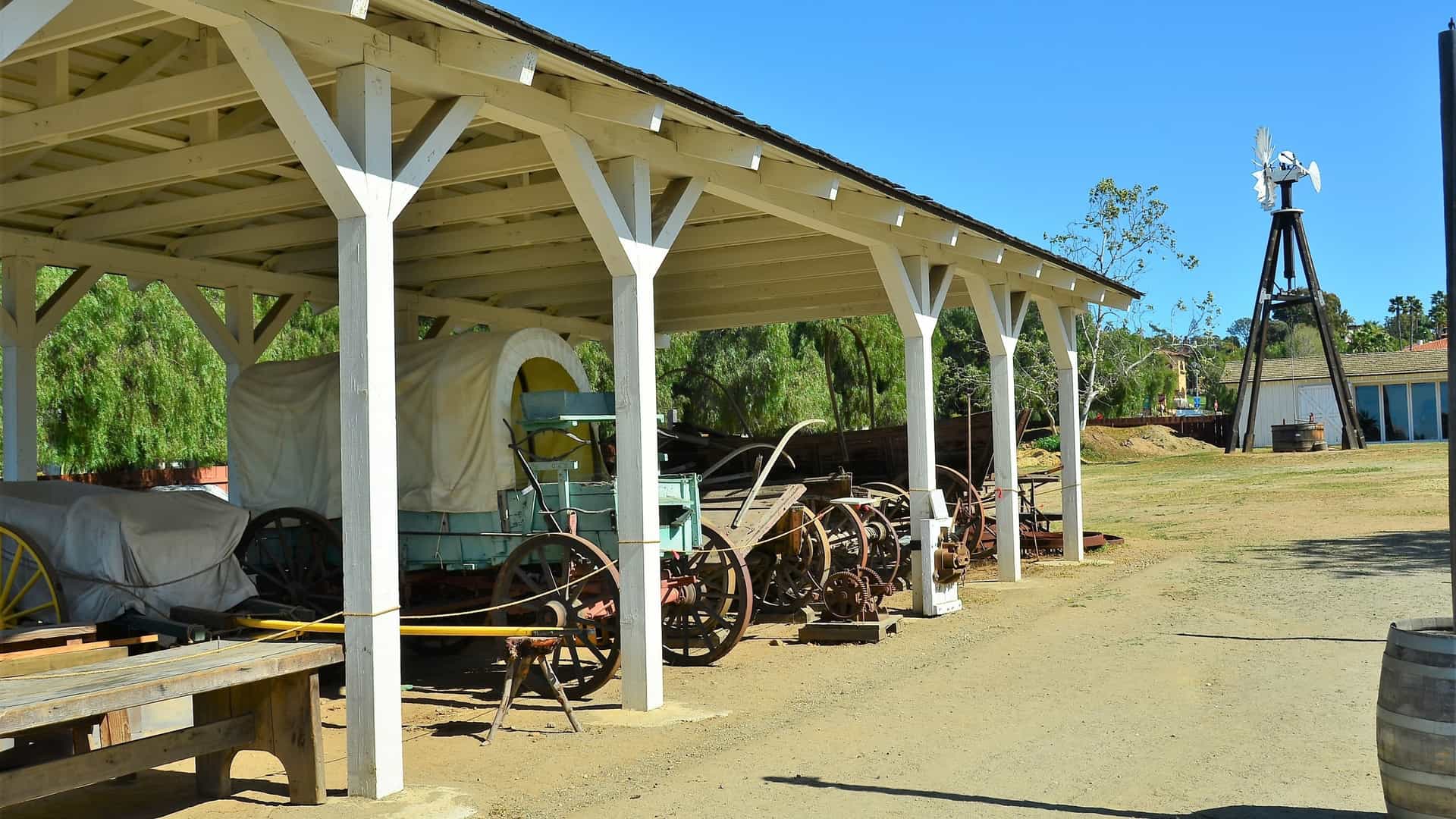 A bright, sunlit street view of the historic Old Town San Diego State Historic Park in California, USA, featuring preserved or reconstructed adobe style buildings with red tile roofs, stucco walls, and wooden balconies, reflecting the area's rich Mexican and early American heritage.