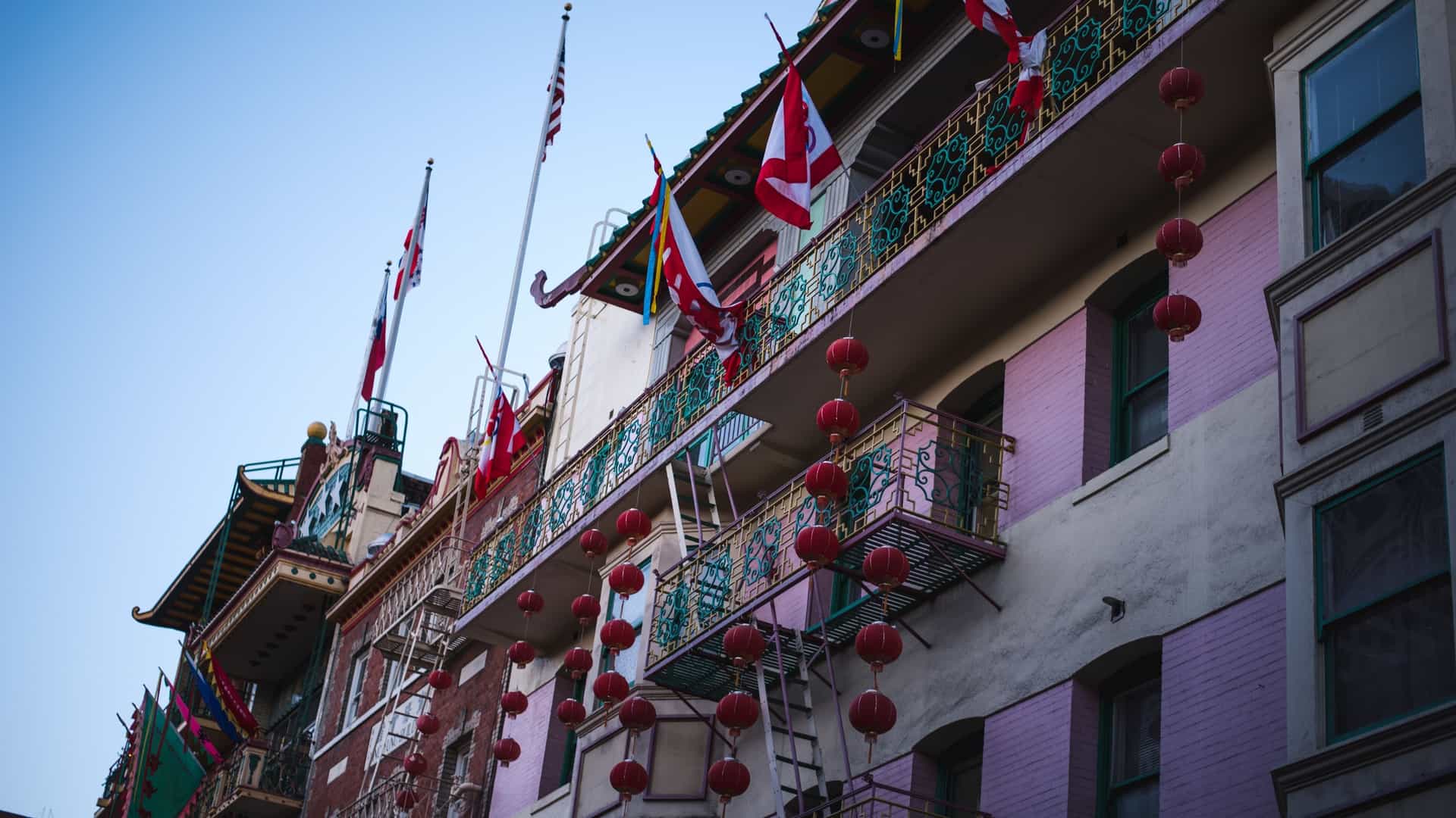 A view looking down a street in San Francisco's Chinatown on an early morning, featuring traditional Chinese architectural details, colorful buildings, and a canopy of red lanterns strung across the street, with minimal pedestrian or vehicle traffic.