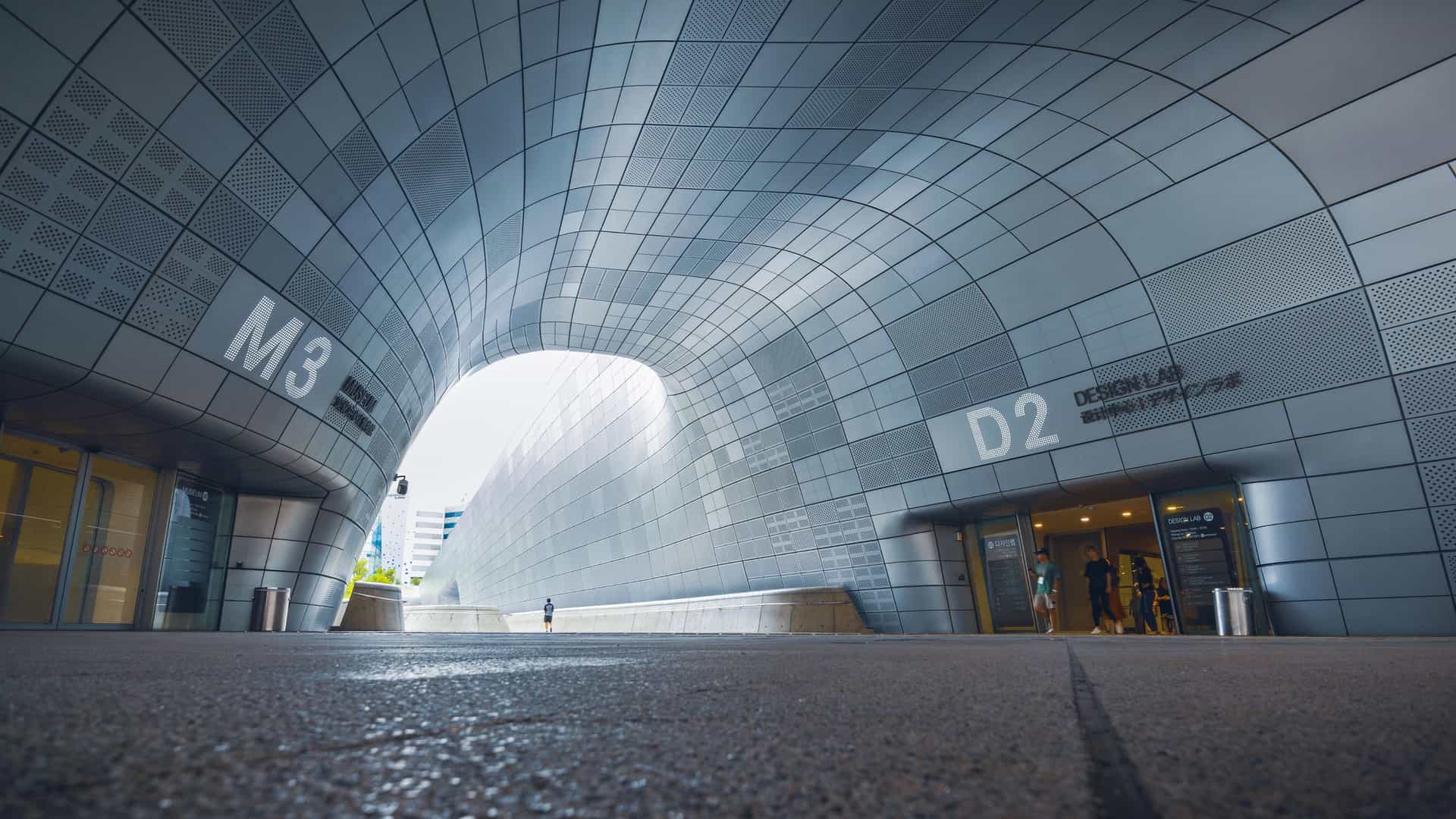 The Dongdaemun Design Plaza (DDP) in Seoul, South Korea, is a massive, futuristic urban landmark designed by Zaha Hadid. The building features a striking, amorphous, and fluid like shape, covered entirely in a seamless facade of thousands of curving, sleek metallic panels.