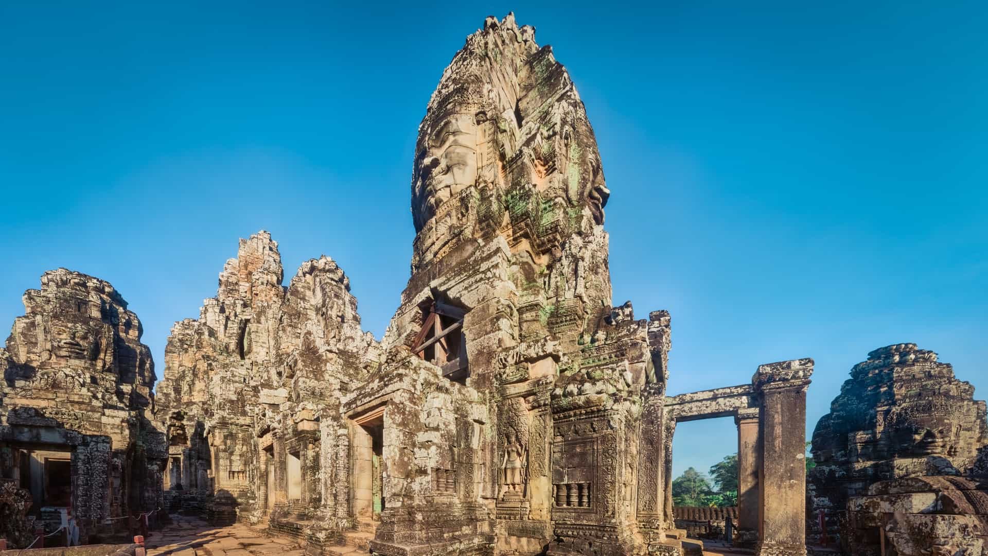 The colossal, four sided smiling stone faces of the Bayon Temple in Angkor Thom, Siem Reap, Cambodia, are illuminated by the soft light of the morning. The dense cluster of stone towers, each adorned with massive, serene faces, defines this unique, ancient Khmer Buddhist monument.