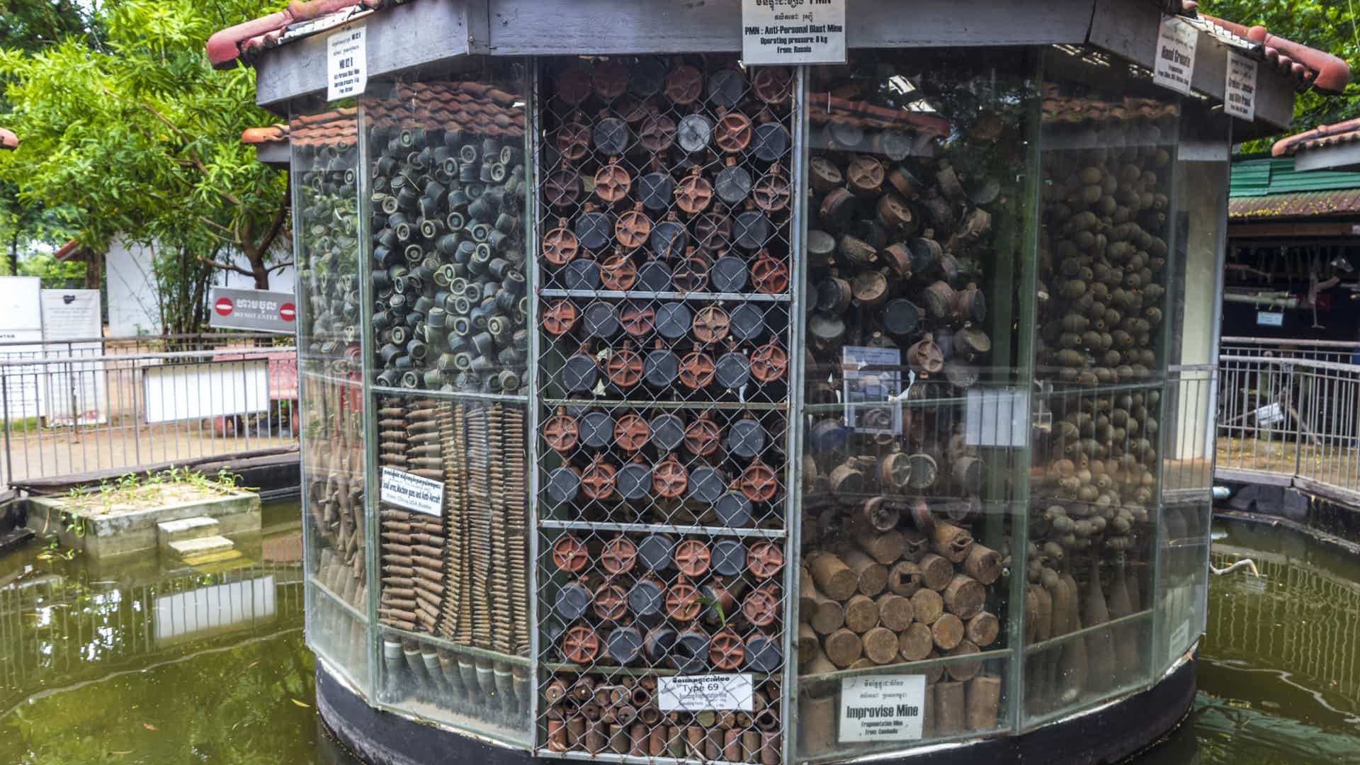 A close up view of a large collection of various types of defused landmines and unexploded ordnance, including both anti personnel and anti tank mines, displayed on the ground at the Cambodia Landmine Museum. The collection features devices of different shapes and colors, highlighting the pervasive danger of post conflict weaponry.