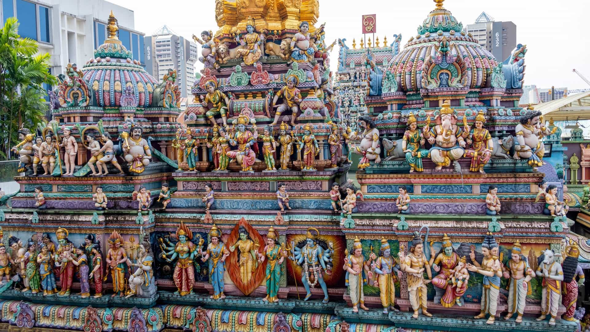 A close up view of the majestic, multi tiered gopuram (ornate tower entrance) of the Sri Veeramakaliamman Temple in Little India, Singapore. The tower is completely covered in hundreds of intricate, brightly painted sculptures depicting various Hindu deities and mythological figures.
