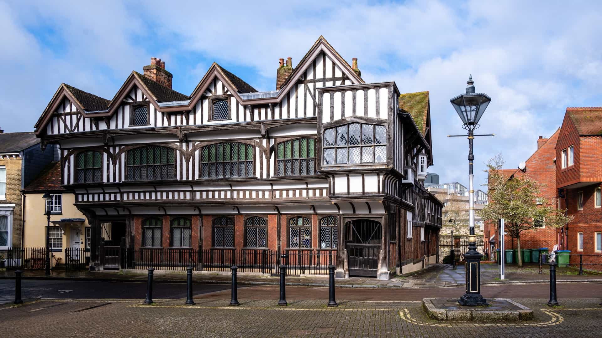 A clear photograph of the famous Tudor House and Garden in Southampton, England, showcasing the historic timber framed, black and white facade of the house, which dates back to the late 15th century. The house is viewed from the side of its traditional Tudor knot garden.