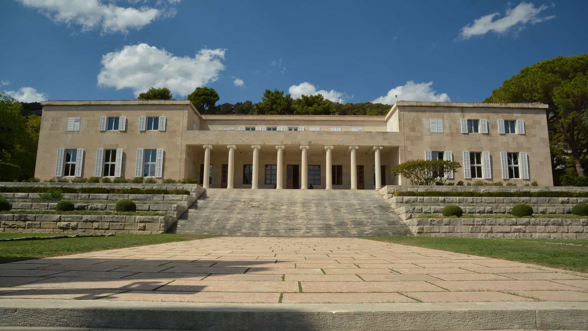The Ivan Meštrović Gallery in Split, Croatia: a symmetrical, light stone building in a classical style with a central colonnaded entrance, viewed from the forecourt across a wide, grand set of stone steps.