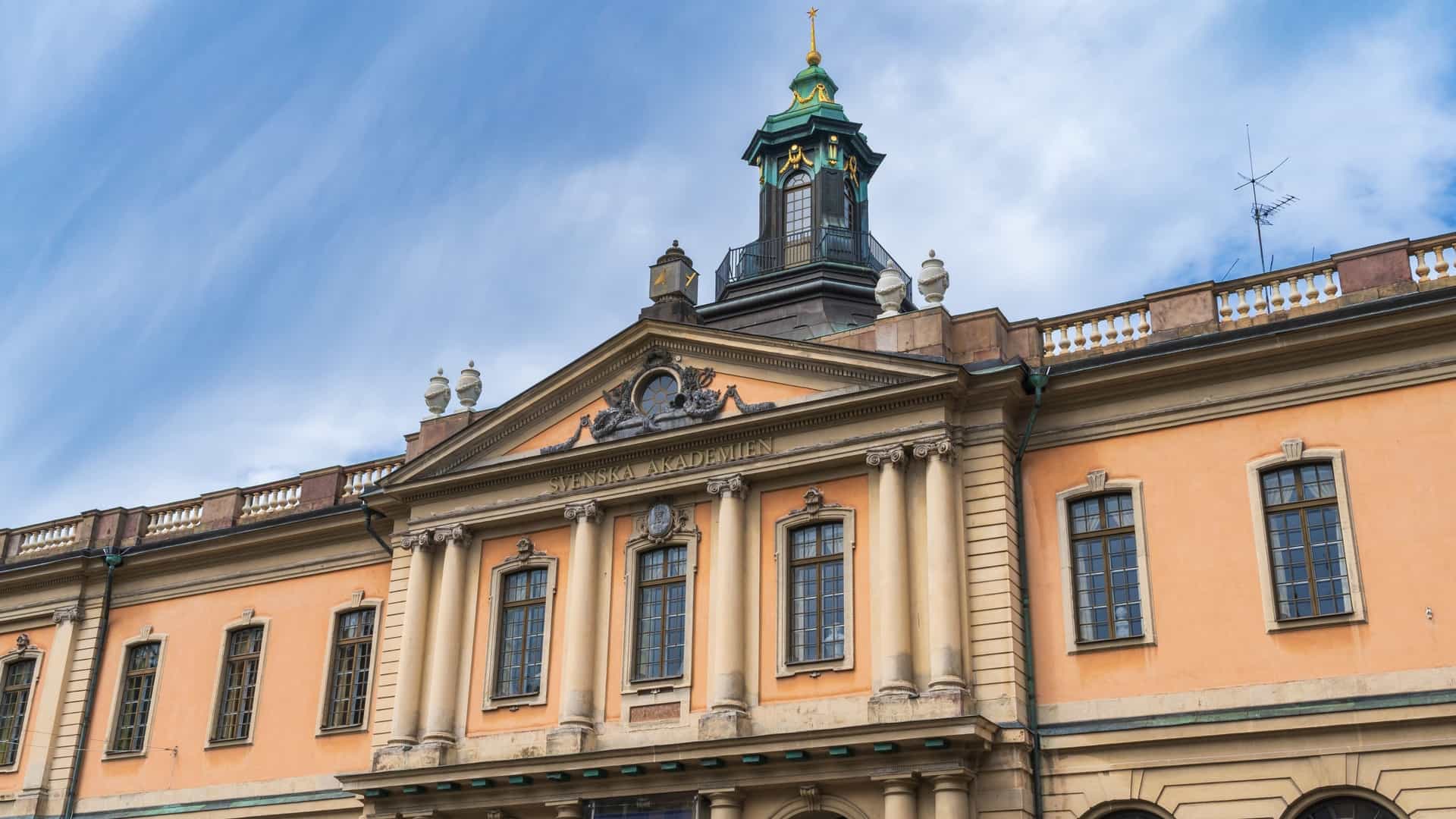 The exterior of the Nobel Prize Museum, housed in the cream colored Börshuset (Stock Exchange Building), situated on Stortorget, the historic cobblestone square in Stockholm's Gamla Stan (Old Town), surrounded by traditional, brightly colored merchant houses.