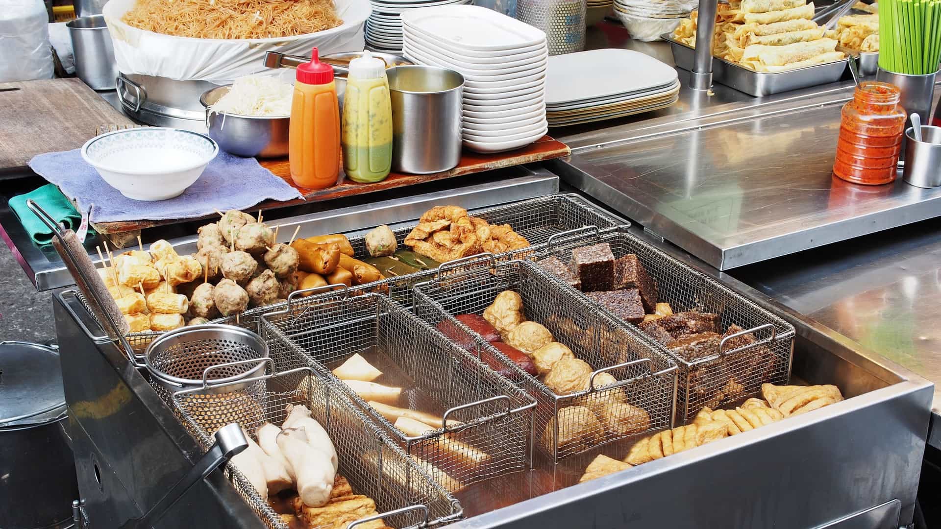 A close up view of a selection of Lu Wei (Taiwanese braised snacks) items displayed under bright lights at a stall in the Keelung Miaokou Night Market in Taiwan. The food, which appears glossy and dark brown from the soy sauce and herb braising liquid, includes hard boiled eggs, tofu, kelp, and various pieces of meat and offal, ready to be sliced and served.