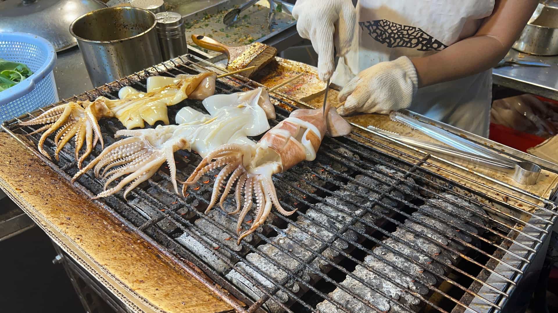 Close up of a street food vendor at a bustling Taiwanese night market, skillfully grilling savory squid skewers over a charcoal fire.