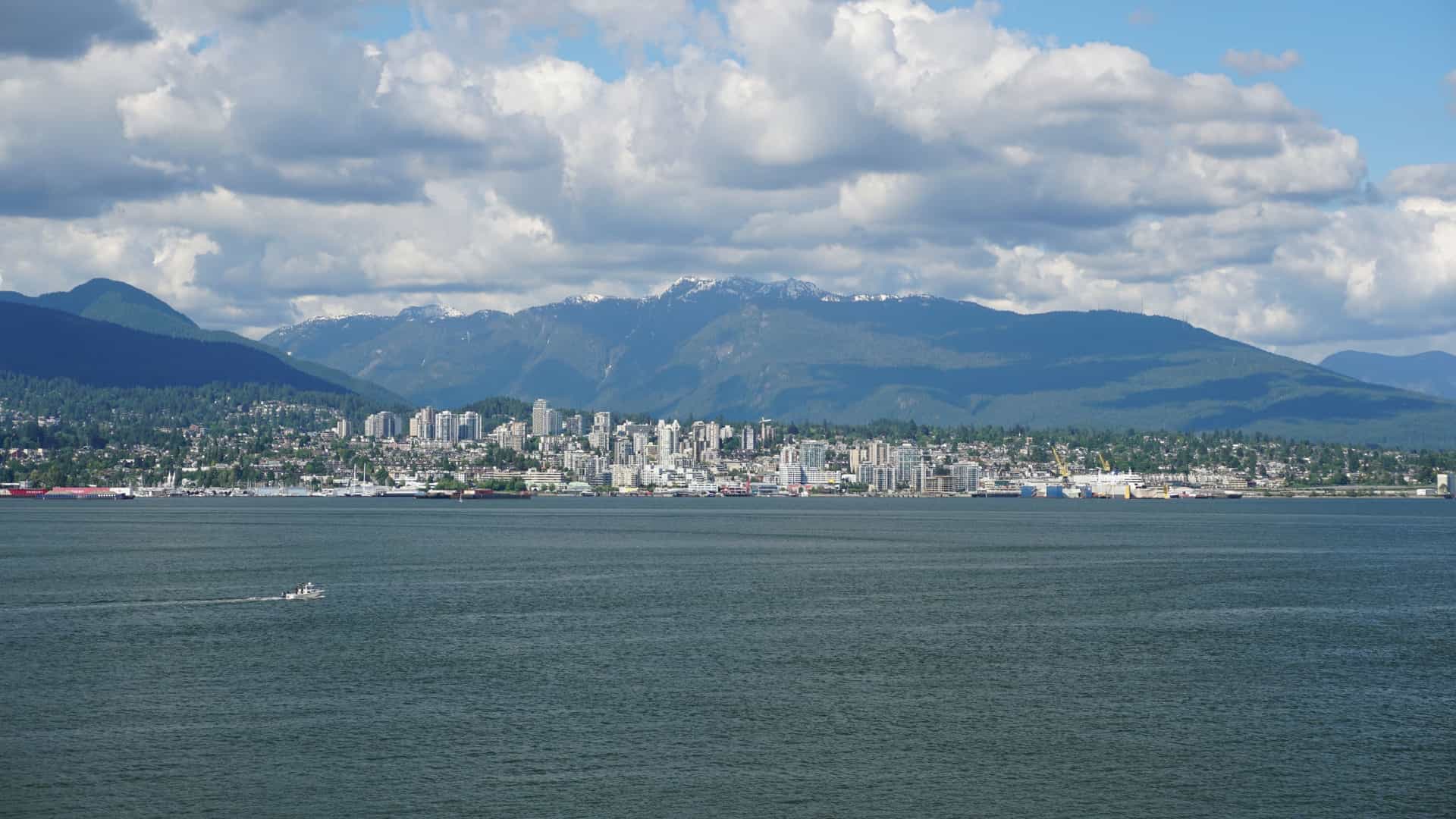 A scenic view of the Thunder Bay waterfront, known as Prince Arthur's Landing. The foreground features modern park amenities, public art installations, and the marina filled with docked boats on Lake Superior. The background is dominated by the city skyline and the iconic landform known as the Sleeping Giant across the bay on the horizon.