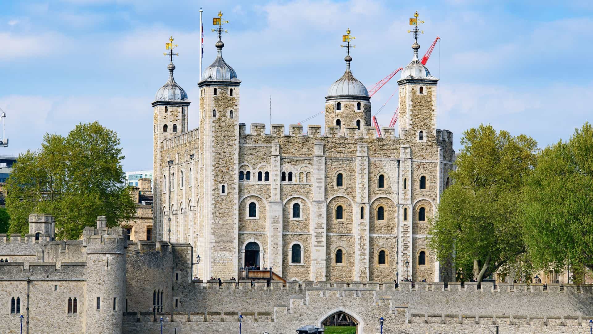 The Tower of London, a historic castle and fortress, is prominently featured on the north bank of the River Thames in central London. The image likely captures the medieval stone walls and the central White Tower, with the river in the foreground, and possibly contrasting modern buildings of the City of London's skyline, such as The Gherkin or The Shard, visible in the background or across the river. The Tower is officially known as His Majesty's Royal Palace and Fortress of the Tower of London and is a UNESCO World Heritage Site.