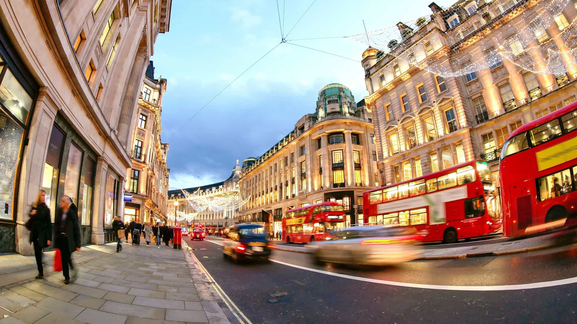 A photograph of Oxford Street in London, showing people shopping on Christmas Day. The street is decorated with festive Christmas lights and decorations, and the image may feature typical London elements such as red double decker buses and black cabs, often depicting a busy scene of shoppers and traffic.