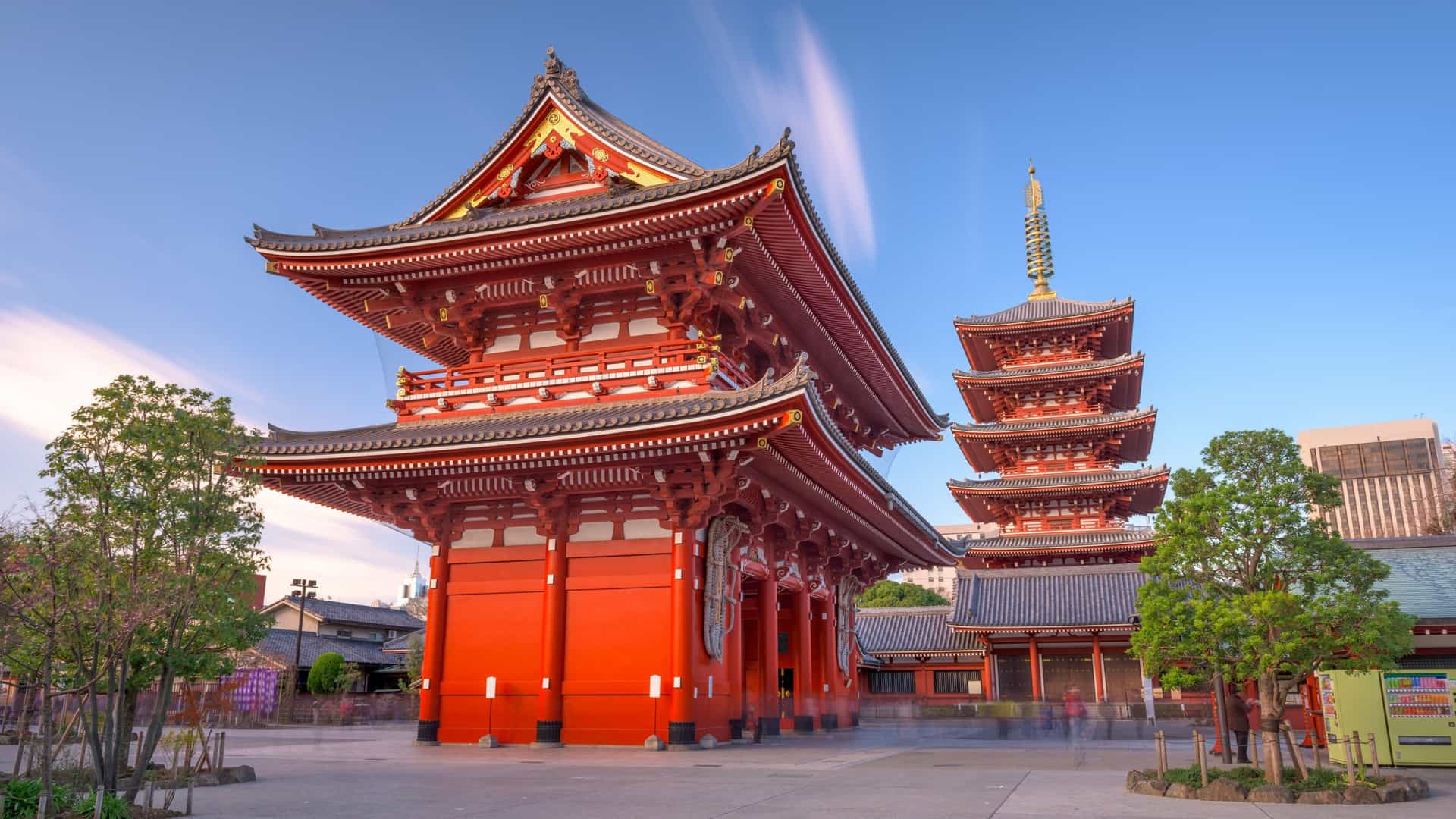 The illuminated Main Hall (Hondo) and Five Storied Pagoda of the Sensoji Temple in Asakusa, Tokyo, at dusk. The temple's vibrant red and dark wood Buddhist architecture is brightly lit, standing out against the twilight sky.