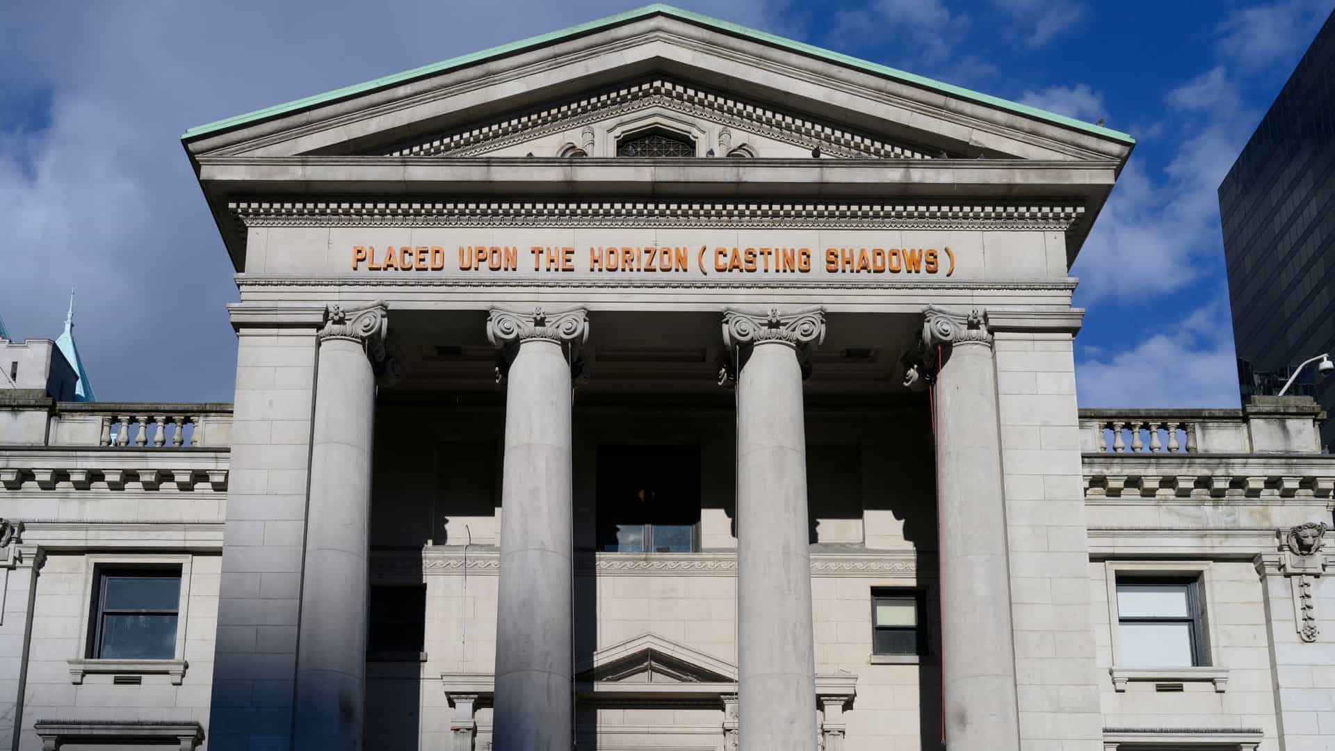 A dramatic, low angle view of the monumental Vancouver Art Gallery in Downtown Vancouver, British Columbia, Canada. The image emphasizes the neo classical architecture of the building, which was formerly a courthouse, featuring large stone columns and a grand entrance. The perspective looks up towards the sky, highlighting the scale of the structure and the clear lines of the architecture.