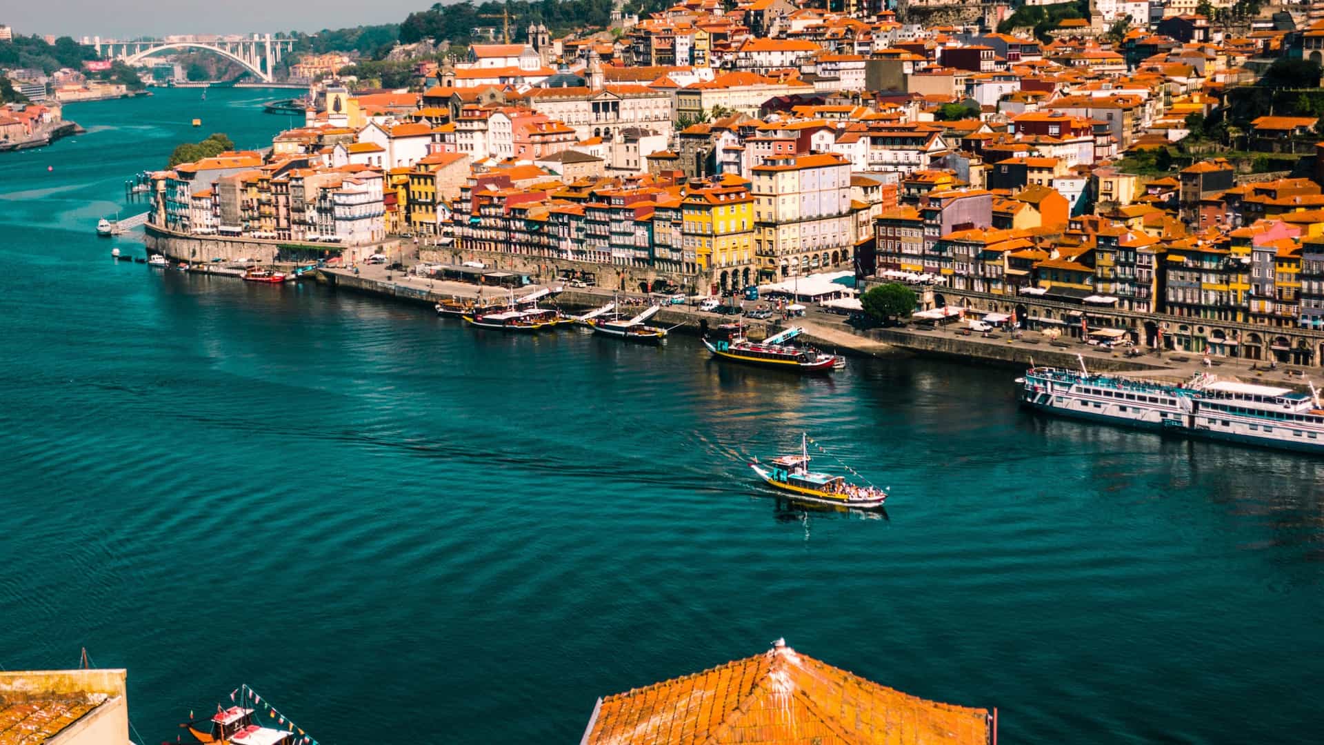 A scenic view of the Douro River as it flows through a region near Salamanca, Spain, likely within the Arribes del Duero Natural Park. A boat navigates the calm water, flanked by steep hillsides covered with green vegetation. The sky is bright with some clouds.