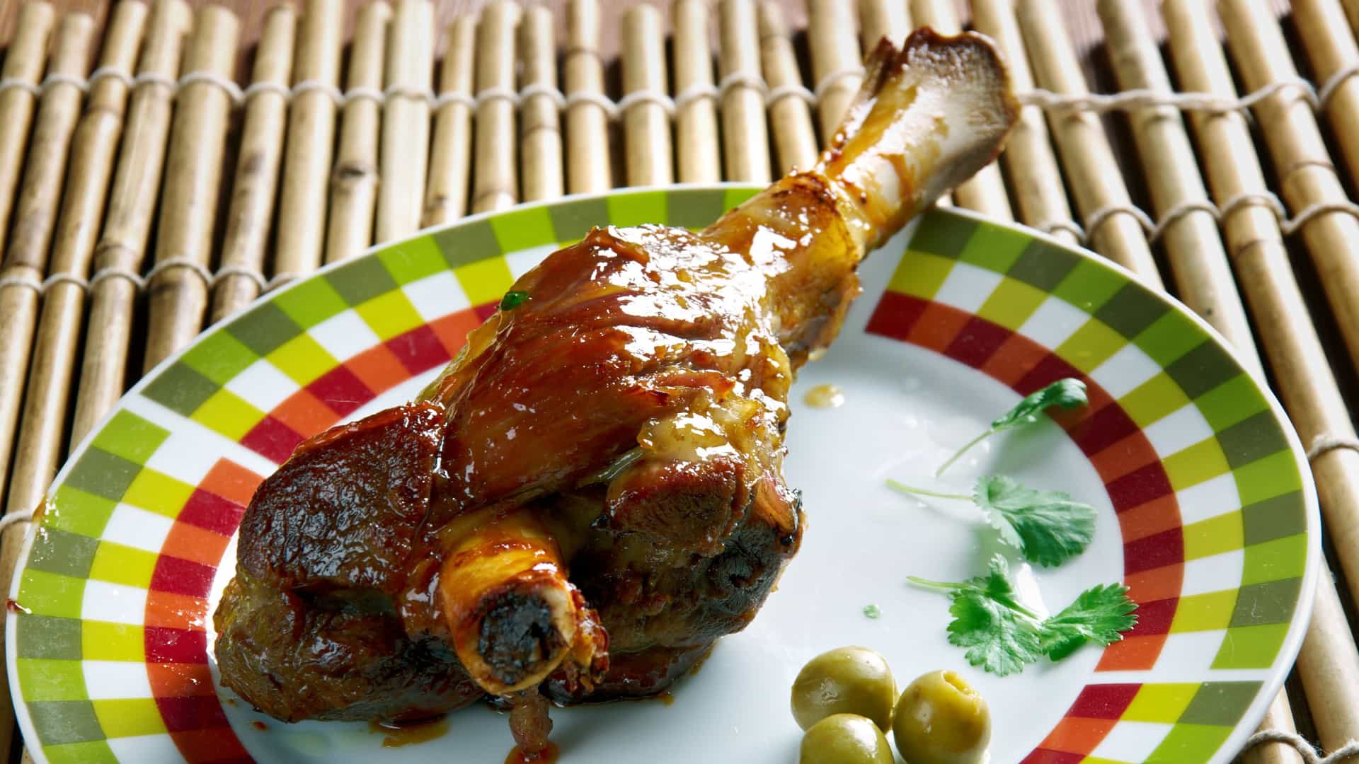 A close up studio shot of a traditional Spanish dish, Lechazo Asado, or roast milk fed lamb. The leg and shoulder of the lamb, cooked to a golden brown and crispy finish, are presented on a white plate. The succulent meat, glistening with natural juices, is garnished simply with coarse salt. This classic dish is typically associated with the Castilla y León region of Spain.
