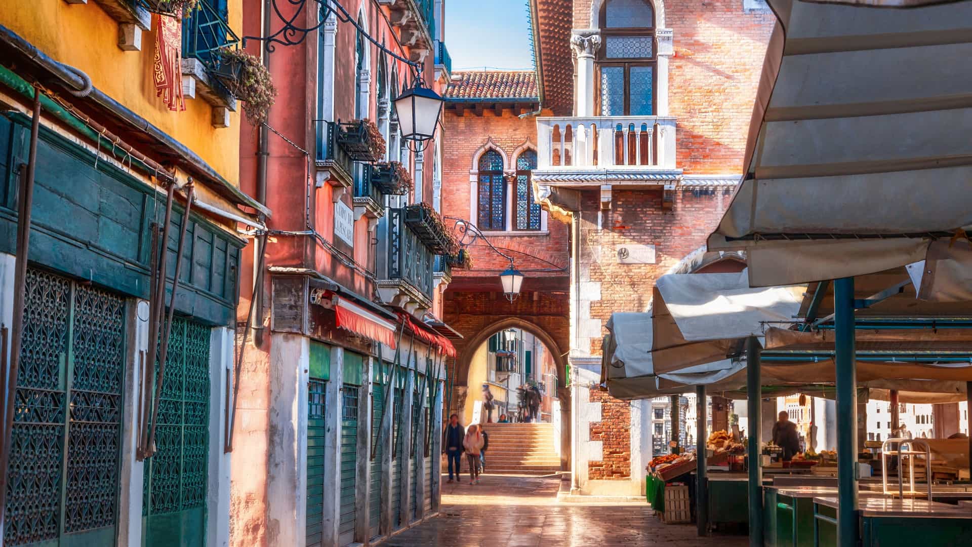 A close up, vibrant scene of the Rialto Fish Market (Pescheria di Rialto) in Venice, Italy. Fresh seafood, including large fish, mussels, clams, and shrimp, is meticulously laid out on ice displays at a market stall. The area is covered by a high, arched, neo Gothic porticoed ceiling, which is part of the historic market structure built in 1907. The image captures the fresh, colorful array of a traditional Venetian fish market.