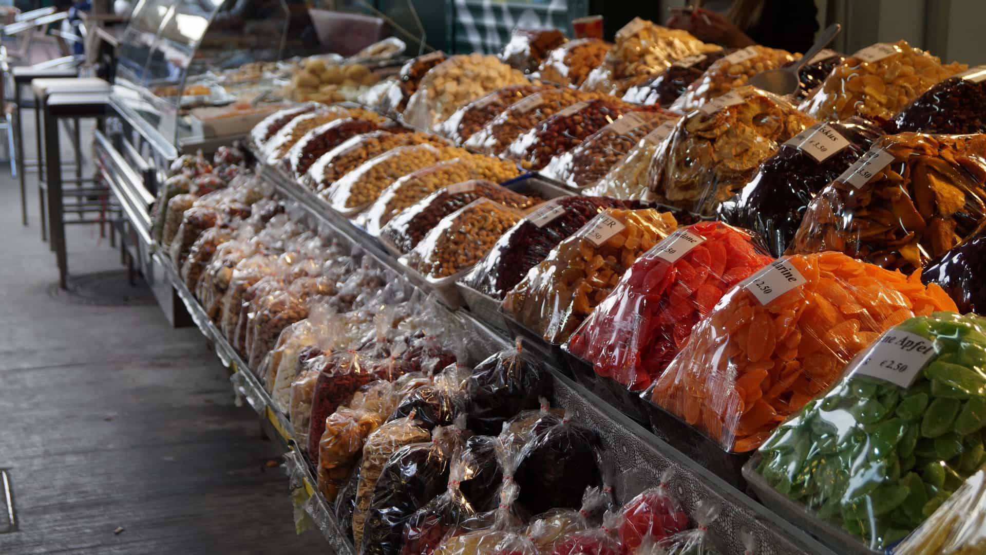 A close up view of a vibrant food stall at the Naschmarkt in Vienna, featuring a colorful and abundant display of various exotic fruits, dried nuts, Middle Eastern spices, and other gourmet delicacies arranged for sale.