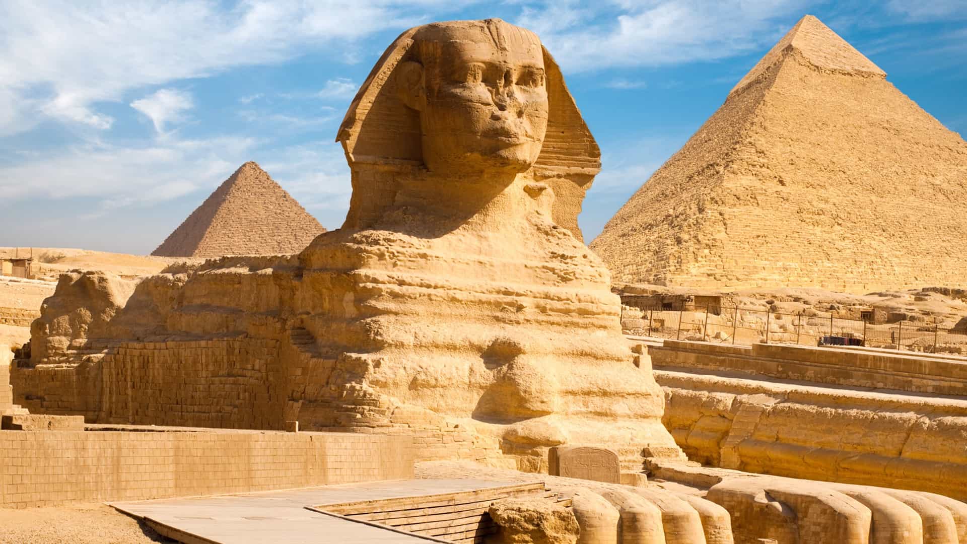 The Great Sphinx with the Pyramids of Giza in the background under a clear blue sky.
