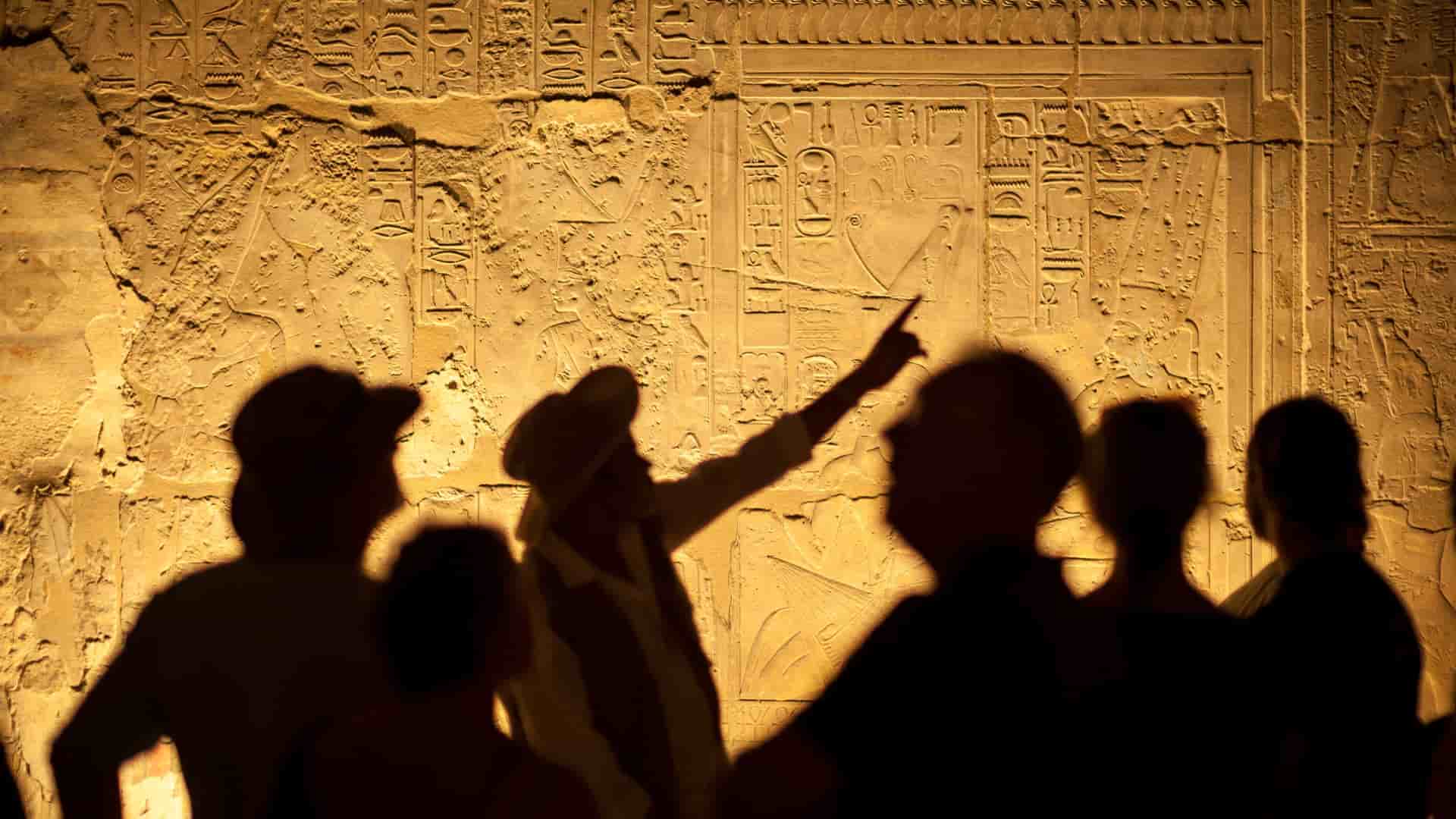 A photo of hieroglyphics in an ancient Egyptian temple with the shadows of a group and tour guide casting along the walls.