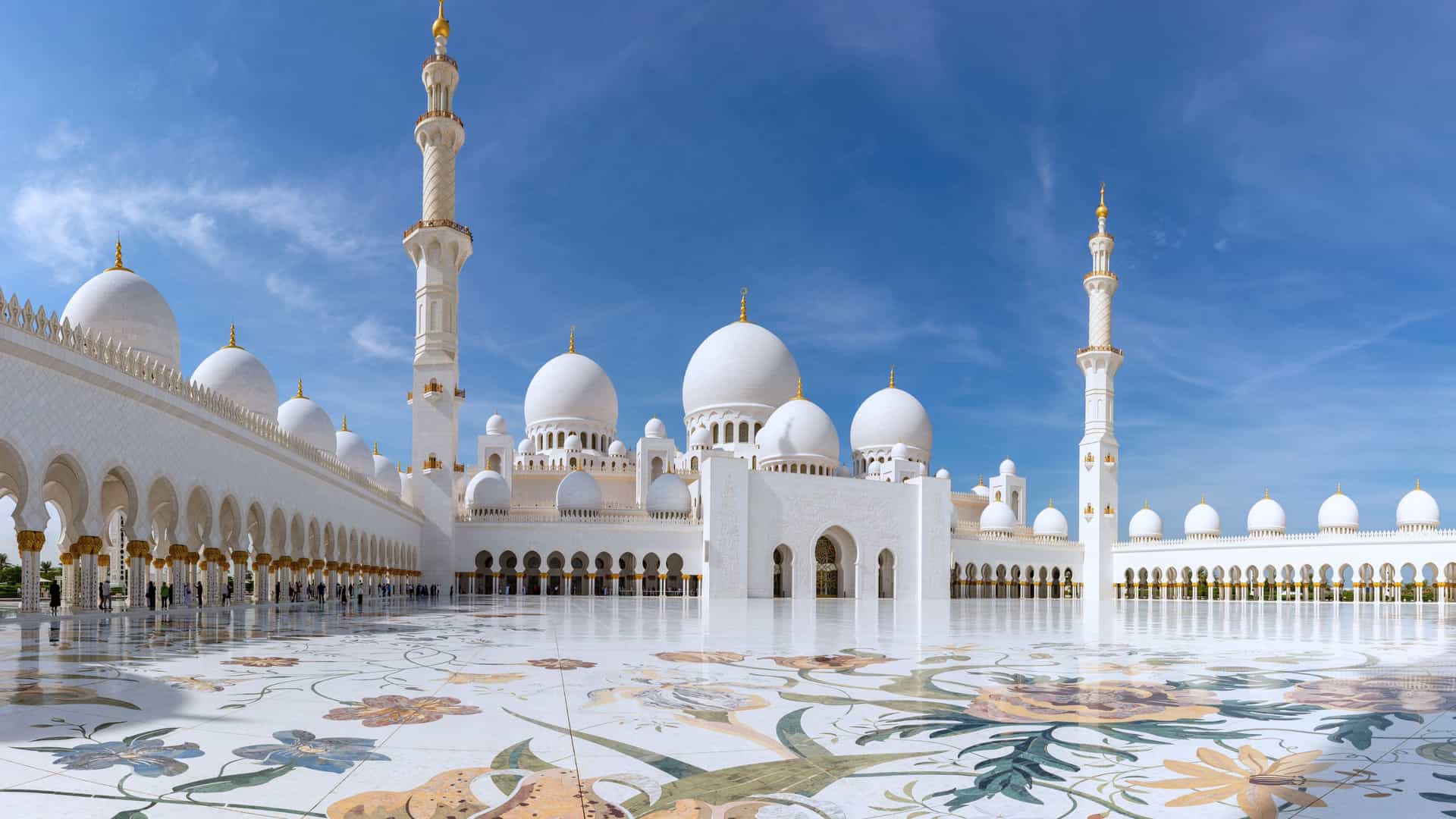 Explora journey view of the grand white marble courtyard and architecture of the Sheikh Zayed Grand Mosque in the Middle East.