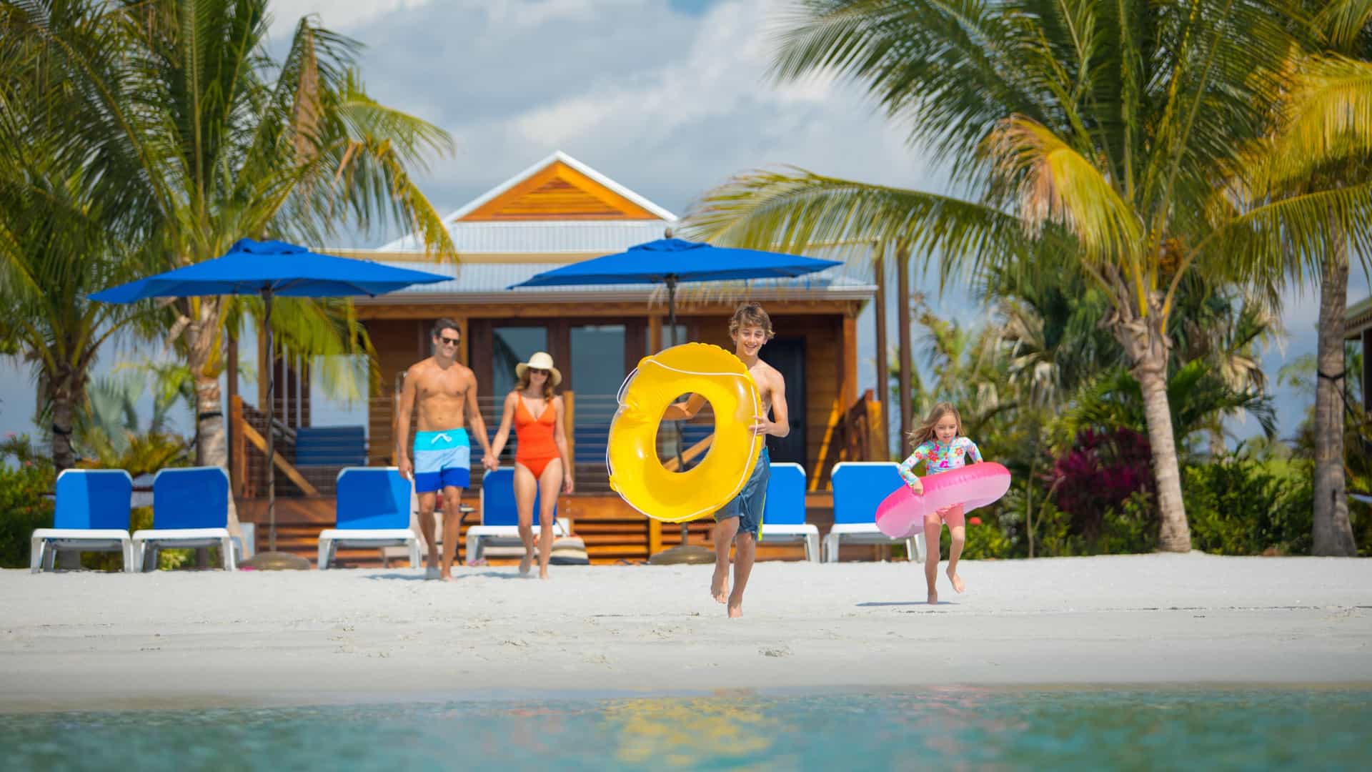 Family playing on beach and running into the water with pool toys.